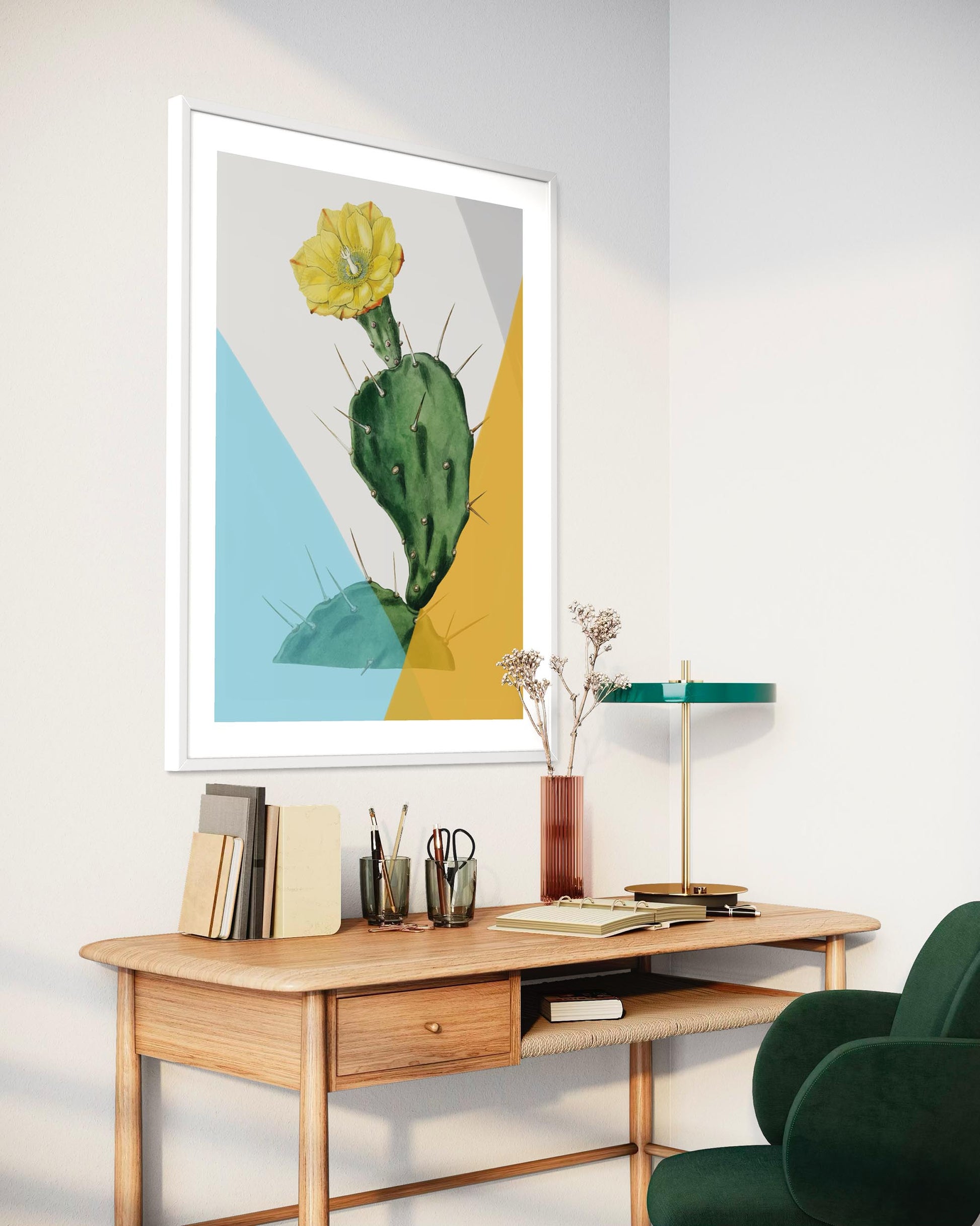 Framed artwork of a cactus on a wall above a desk with books and decor items.