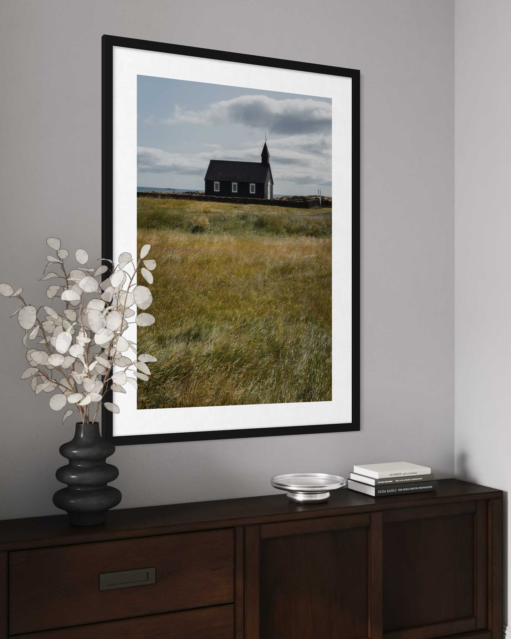 Framed photograph of a church in a field on a gray wall above a wooden console table.