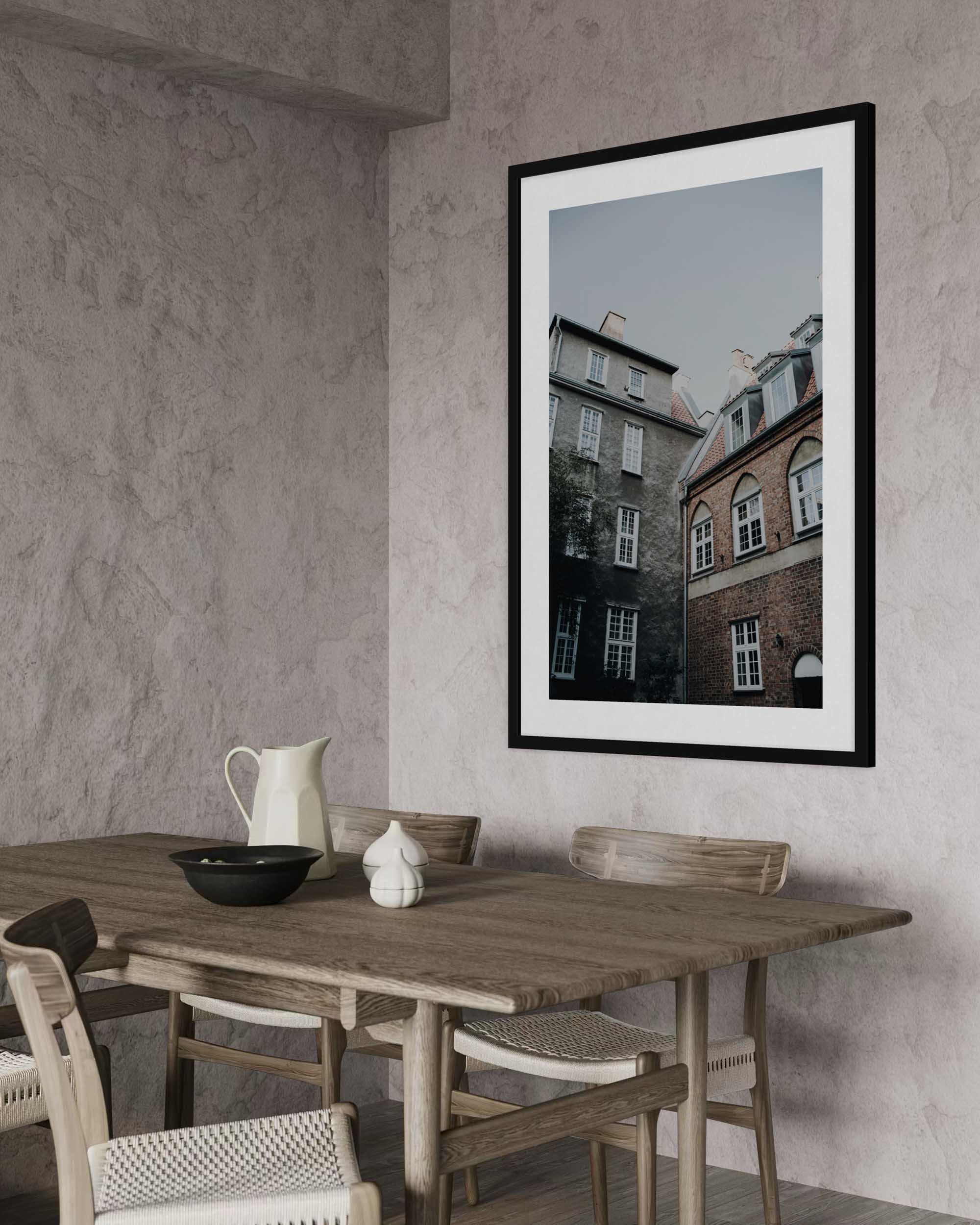Framed artwork of a cityscape above a wooden dining table in a room with gray walls.