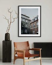 Framed artwork on a wall above a brown leather chair in a room.