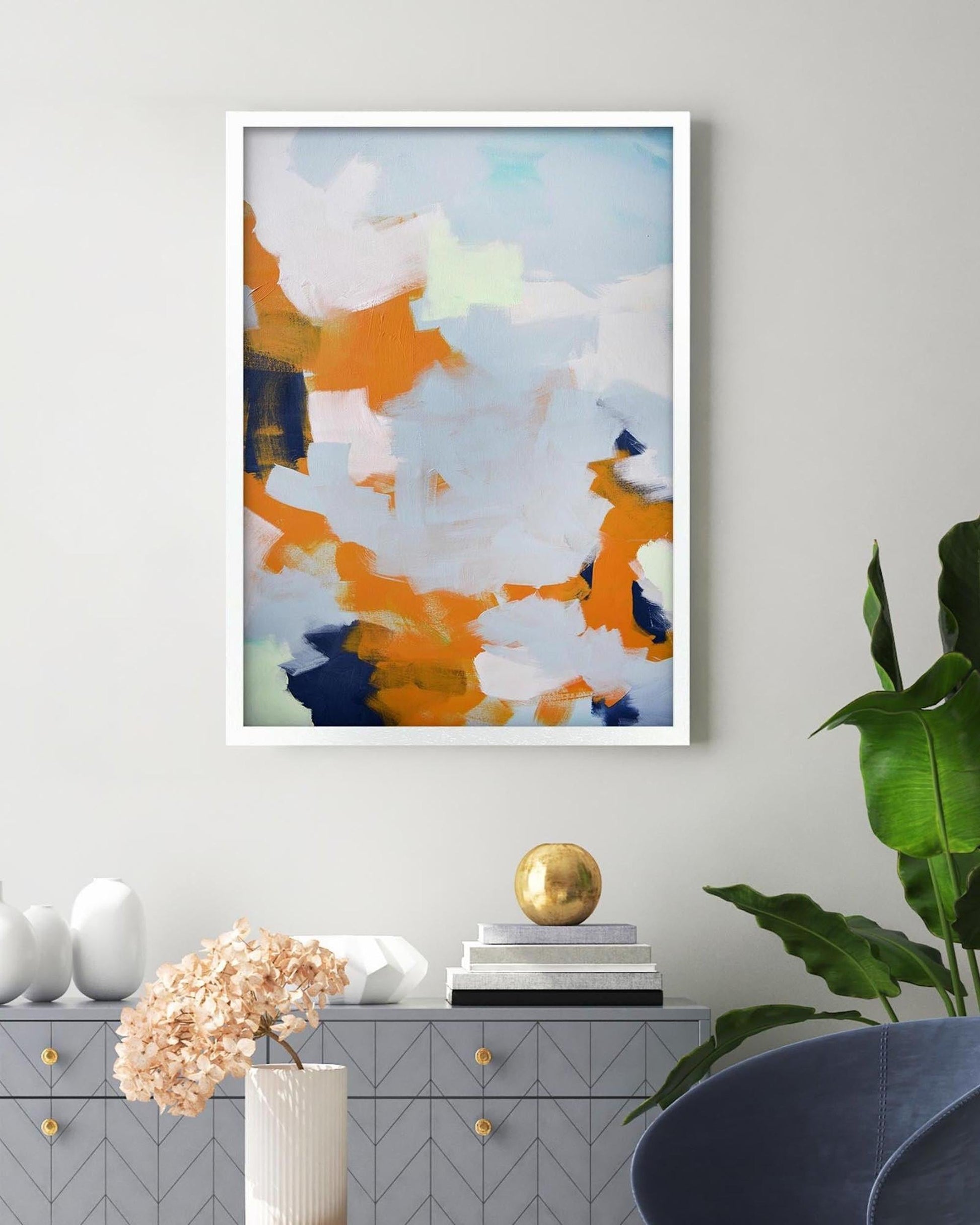 Abstract art print on a wall with a cabinet and plant in the foreground