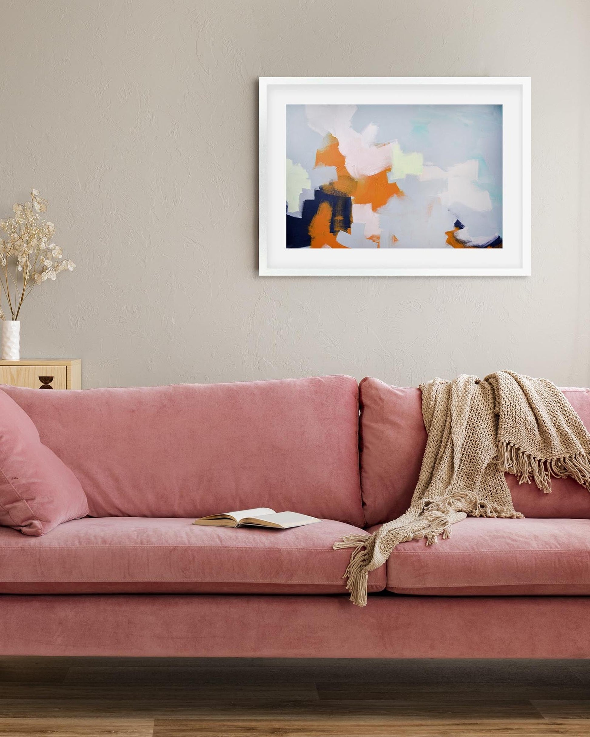 Pink sofa with a blanket and book in a living room with abstract art on the wall.