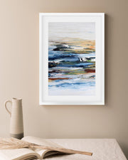 Framed abstract art on a beige wall with a pitcher and book below.