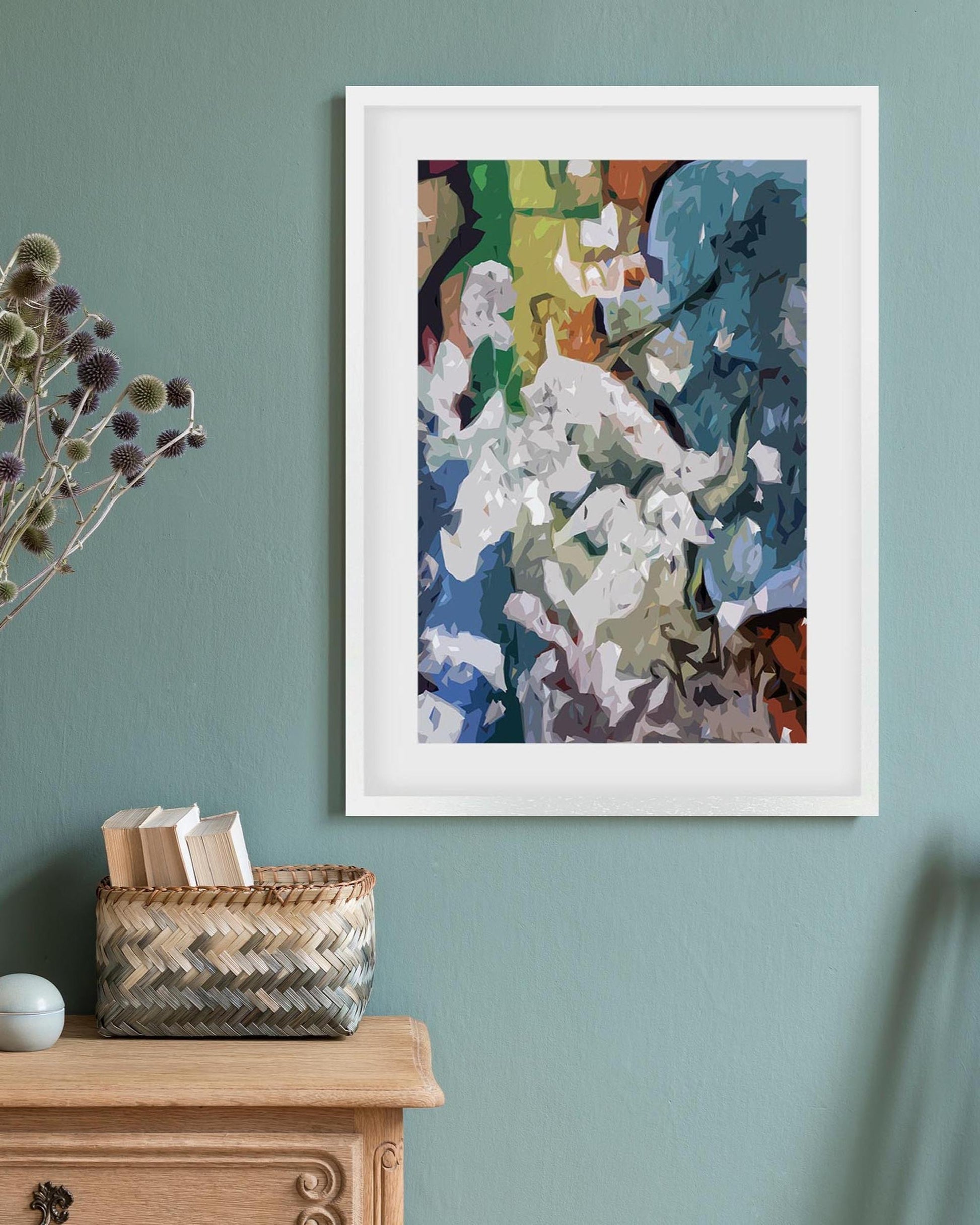 Framed abstract artwork on a teal wall with a wooden cabinet and basket below.