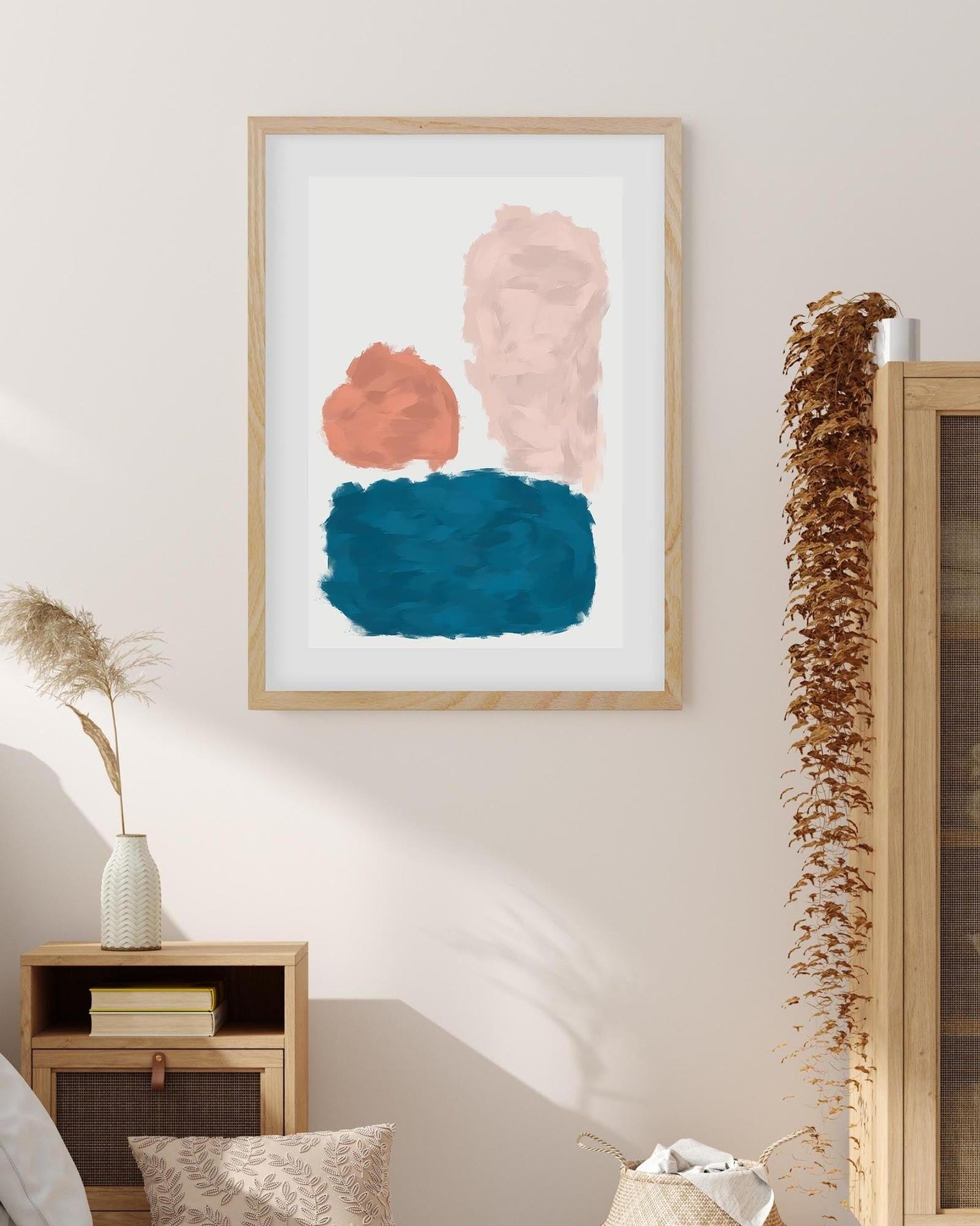 Framed abstract art with pink, blue, and orange colors on a wall above a wooden side table.