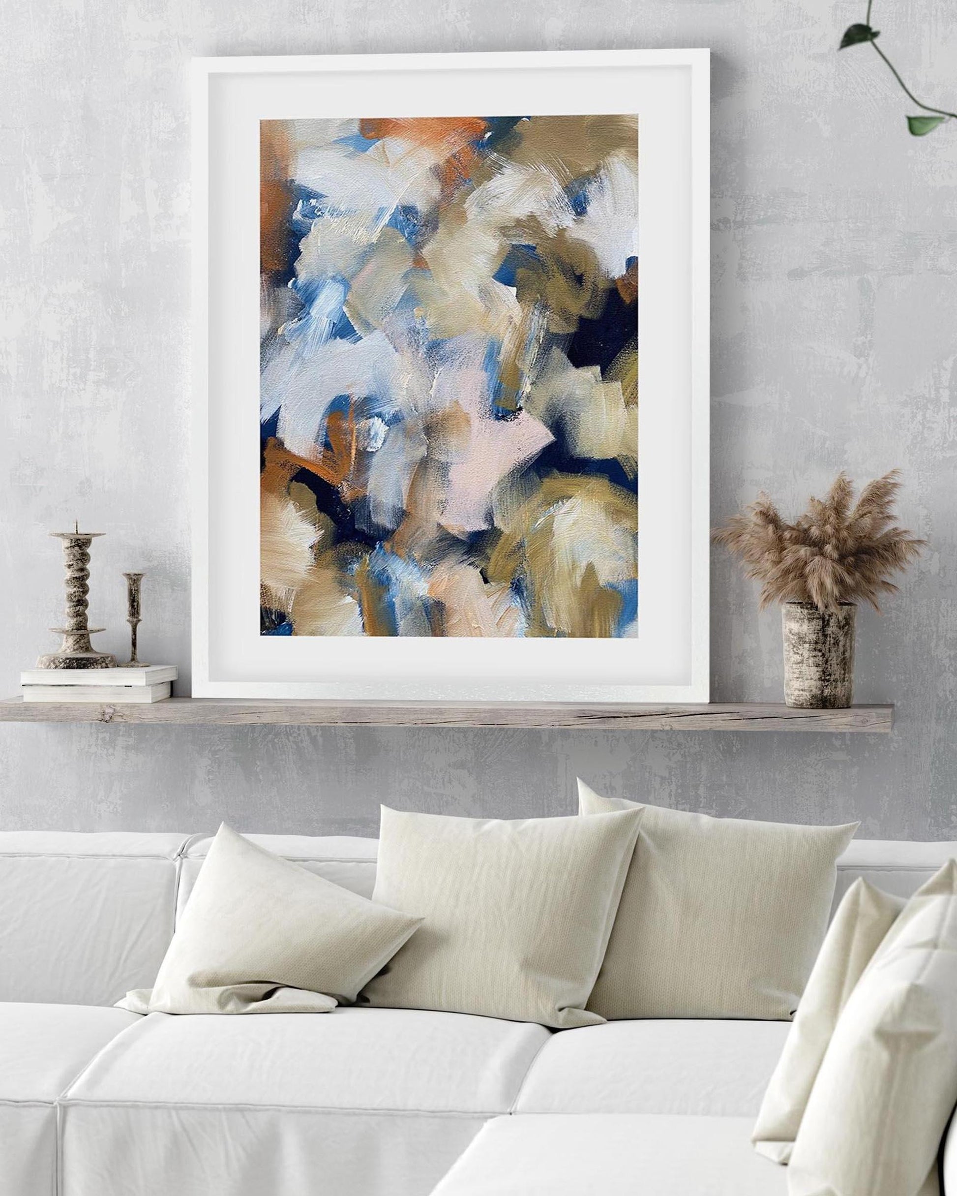 Abstract painting in a white frame on a wall above a sofa with decorative pillows.