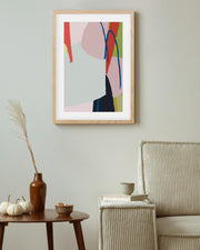 Abstract art print in a wooden frame on a wall above a table with decorative items.