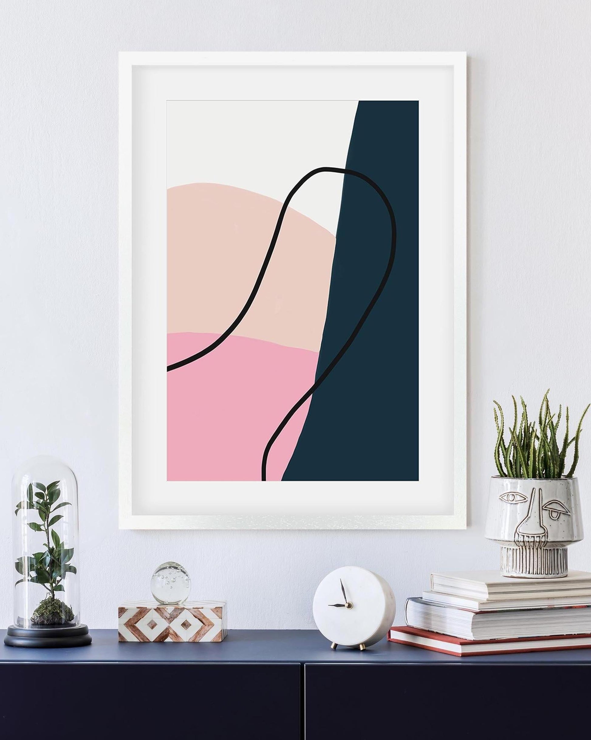 Abstract art print with pink and blue shapes on a white wall above a shelf with decorative items.