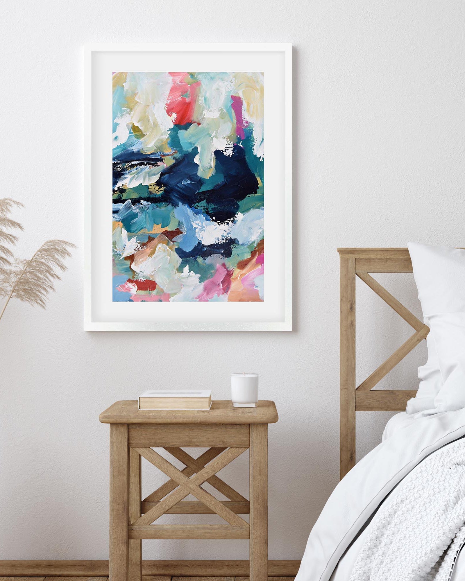 Abstract art print in a white frame on a wall above a wooden side table.