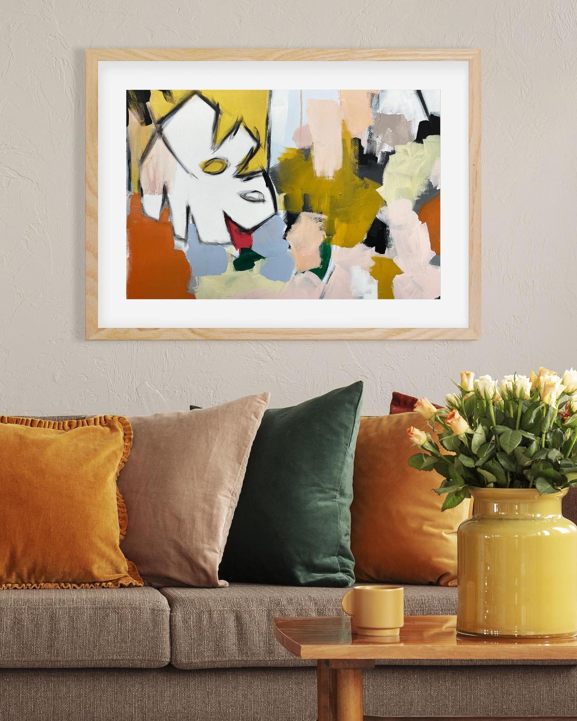 Abstract painting on a wall above a sofa with colorful cushions and a vase of flowers.