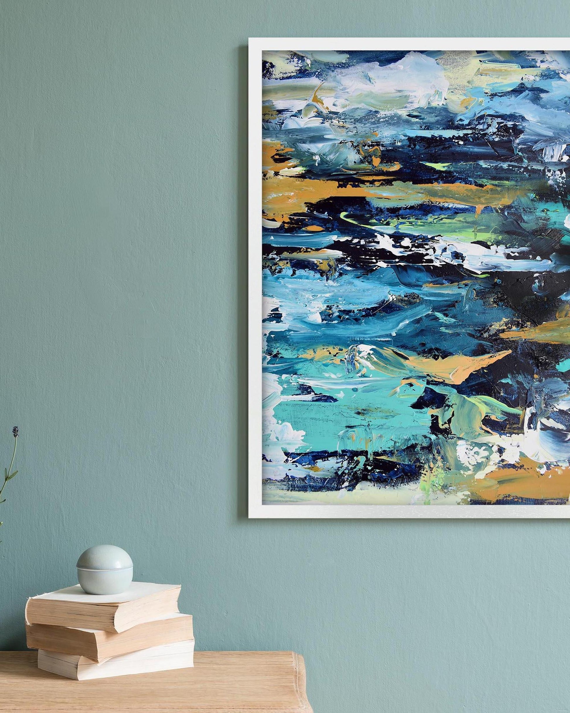 Abstract painting with blue, green, and yellow colors on a light blue wall above a stack of books.