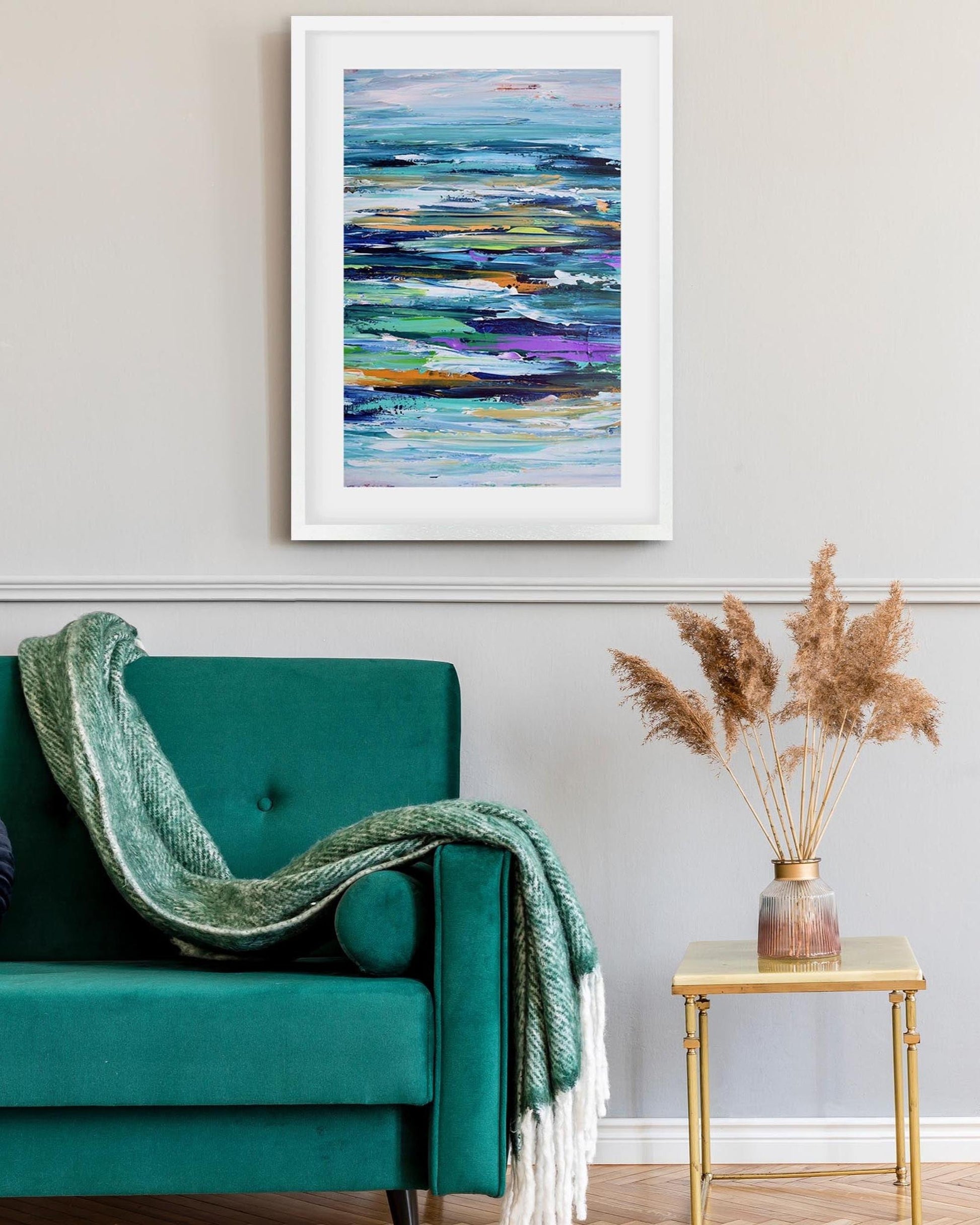 Framed abstract painting on a wall above a teal sofa with a green blanket.