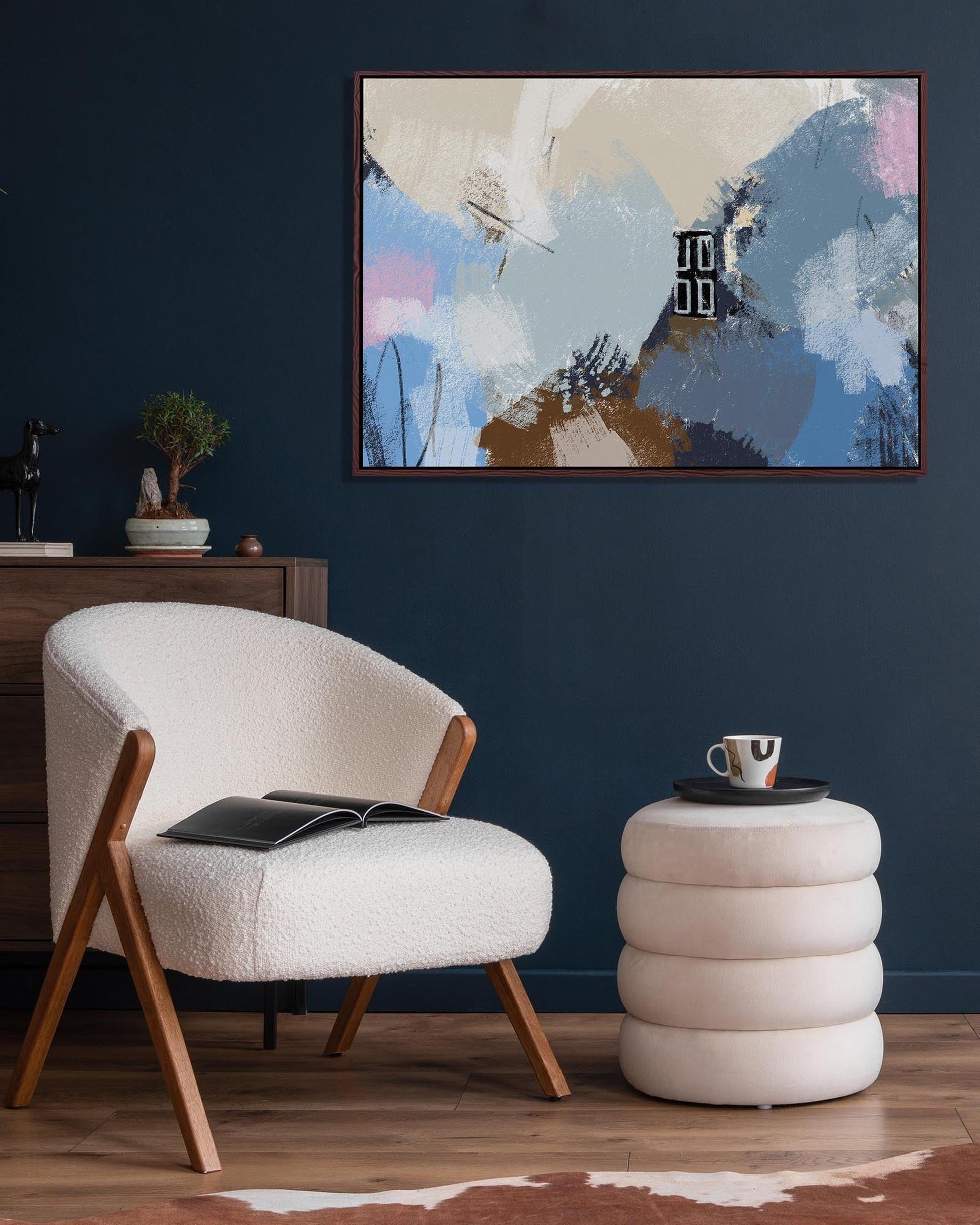 Modern living room with a white armchair, round side table, and abstract painting on a dark blue wall.