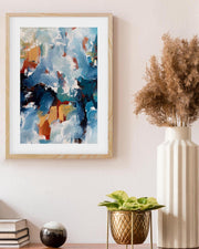 Framed abstract art piece on a wall with decorative plants and books below.
