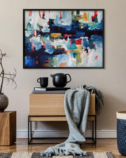 Abstract painting on a wall above a wooden side table with decorative items.