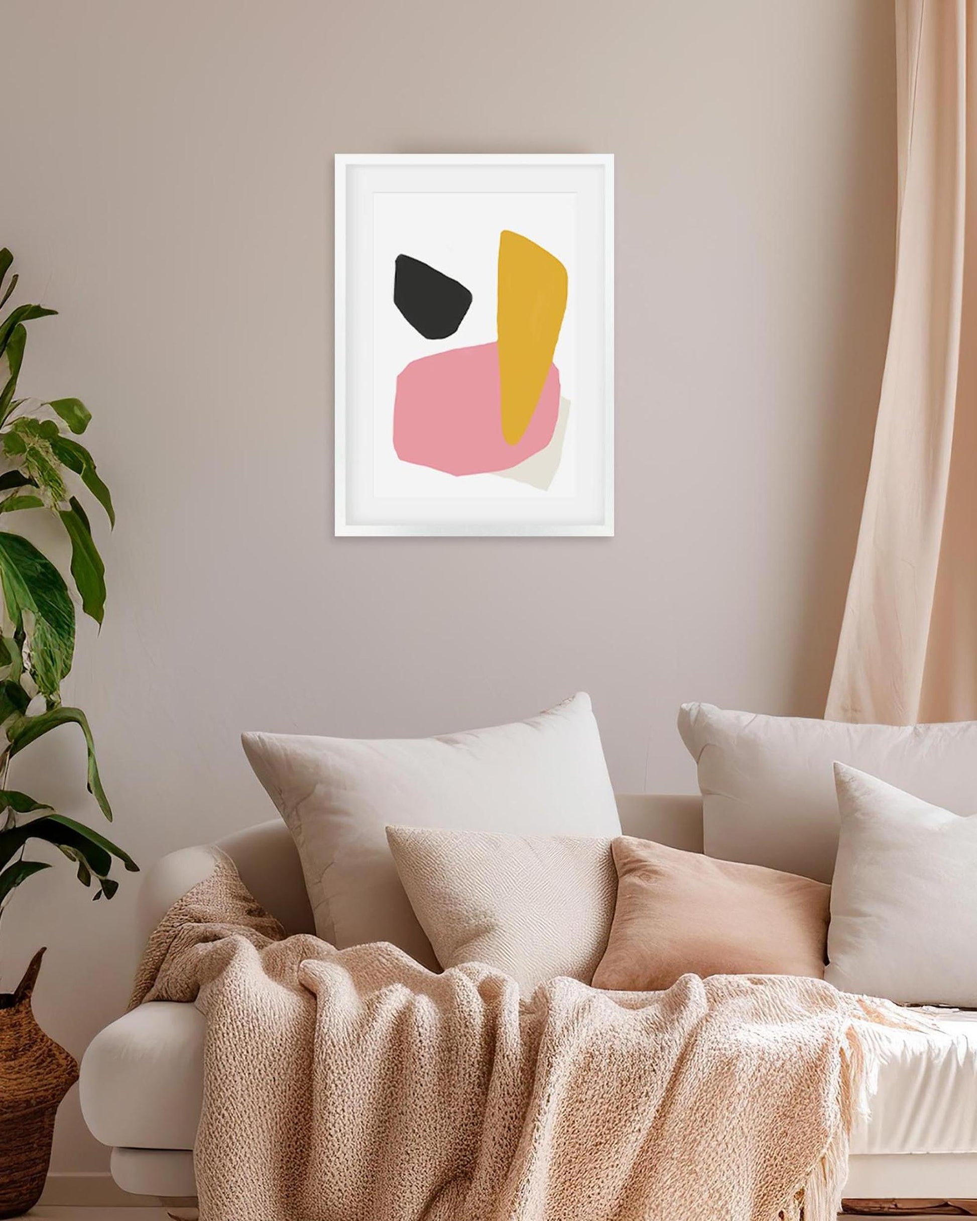 Abstract art print on a wall above a sofa with pillows and a blanket.