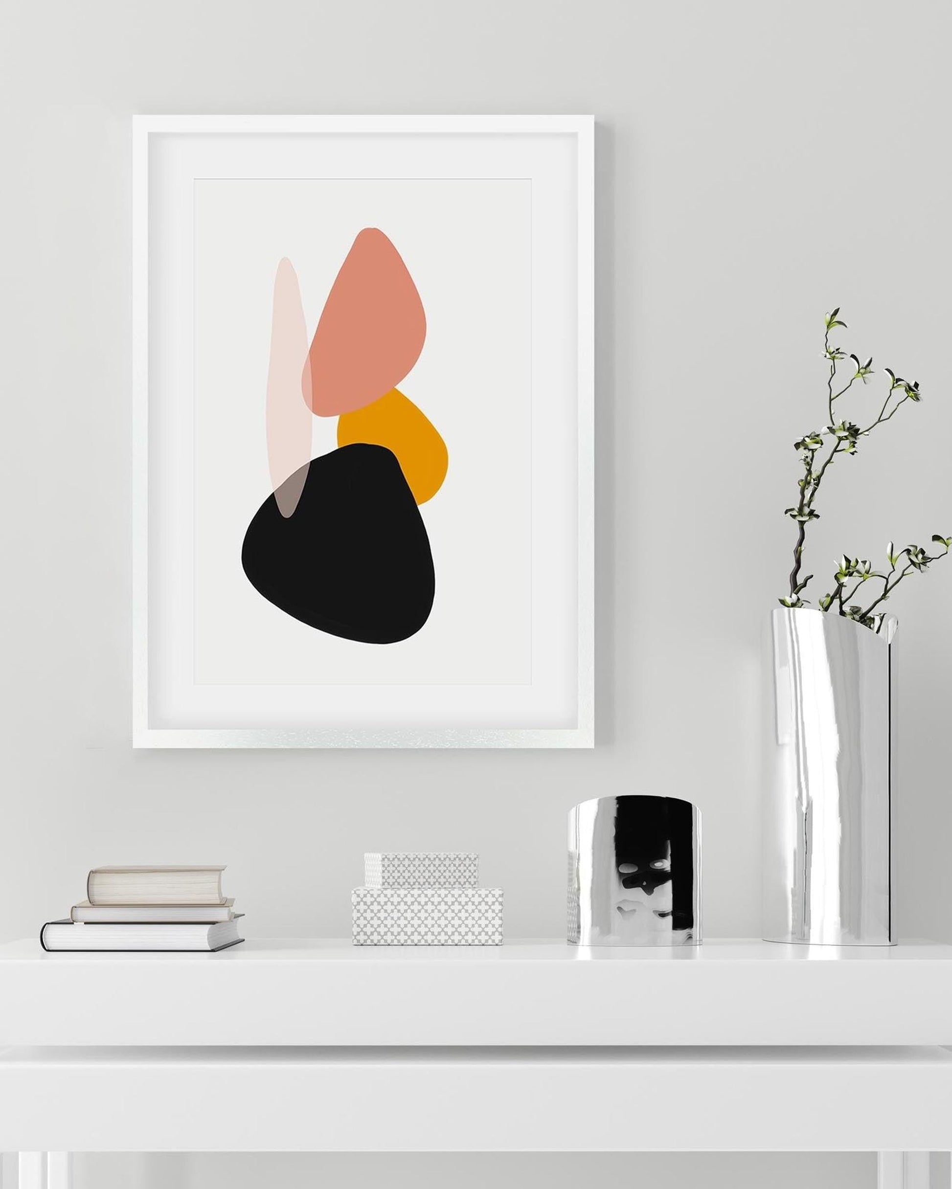 Framed abstract art print on a wall above a white surface with decor items.
