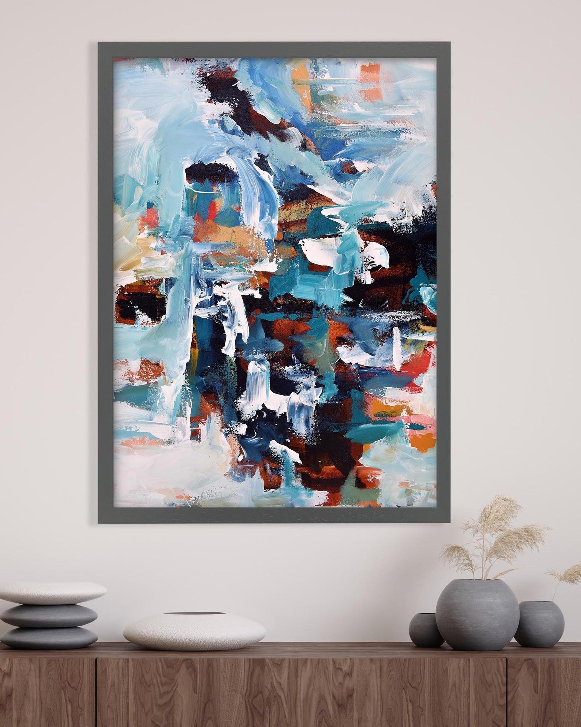 Abstract painting in a gray frame on a wall above a wooden shelf with decorative items.