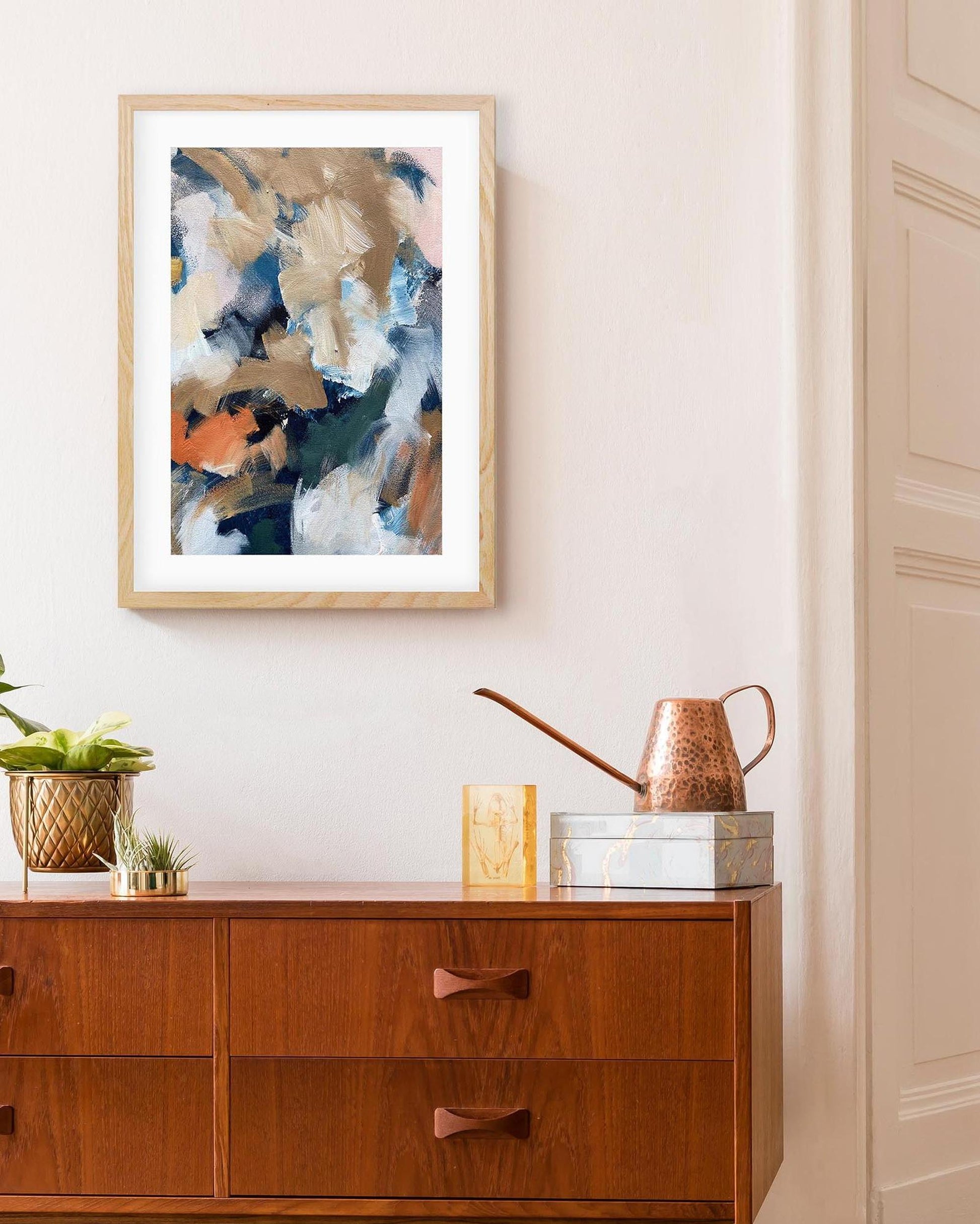 Framed abstract art above a wooden dresser with decorative items.