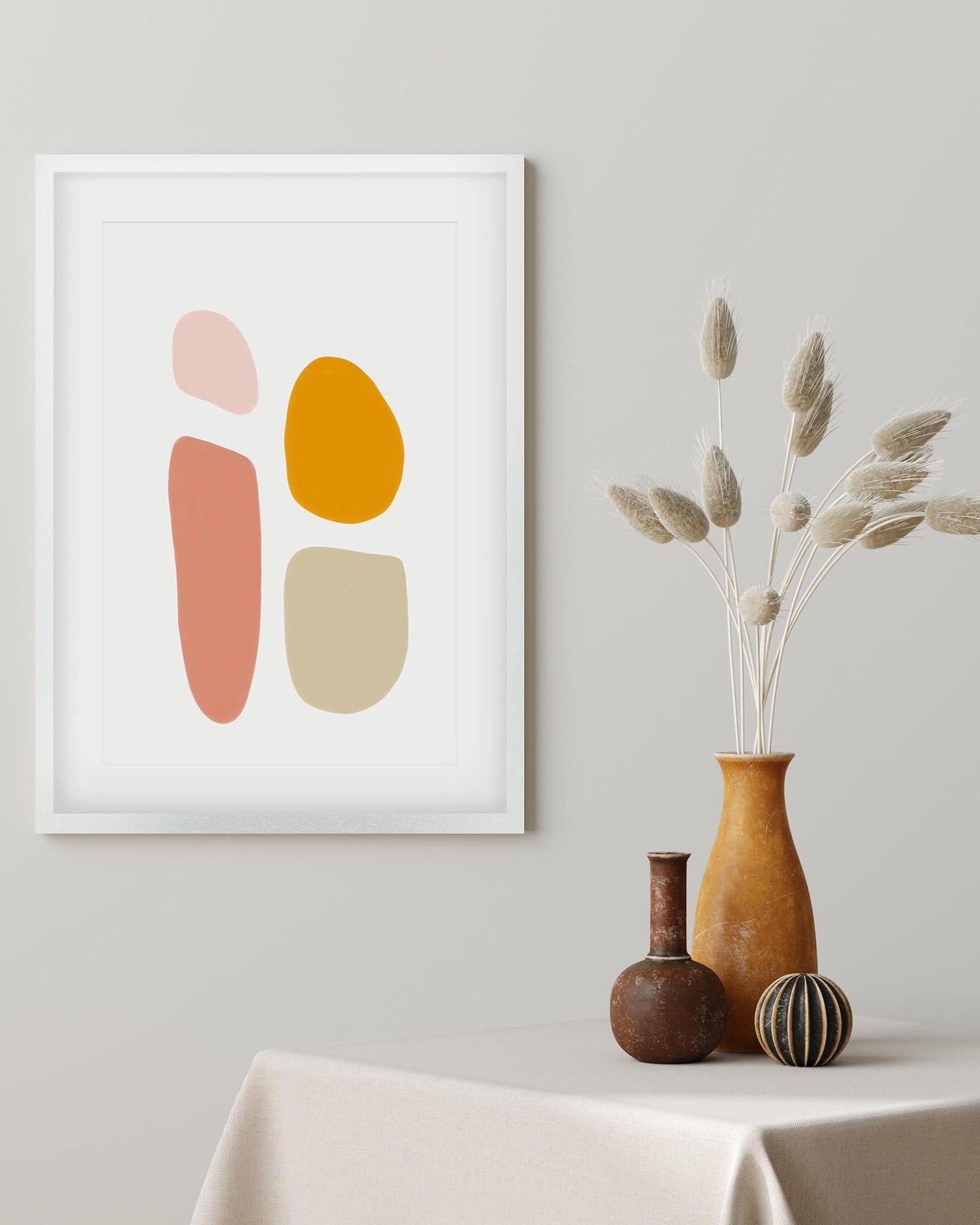 Framed abstract art print with colorful shapes on a wall above a table with decorative vases.