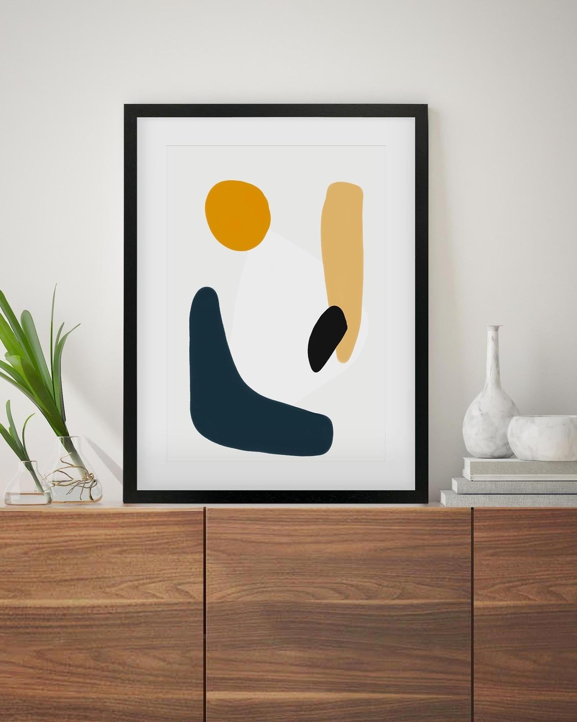 Abstract art print with geometric shapes in a black frame on a wall above a wooden cabinet.