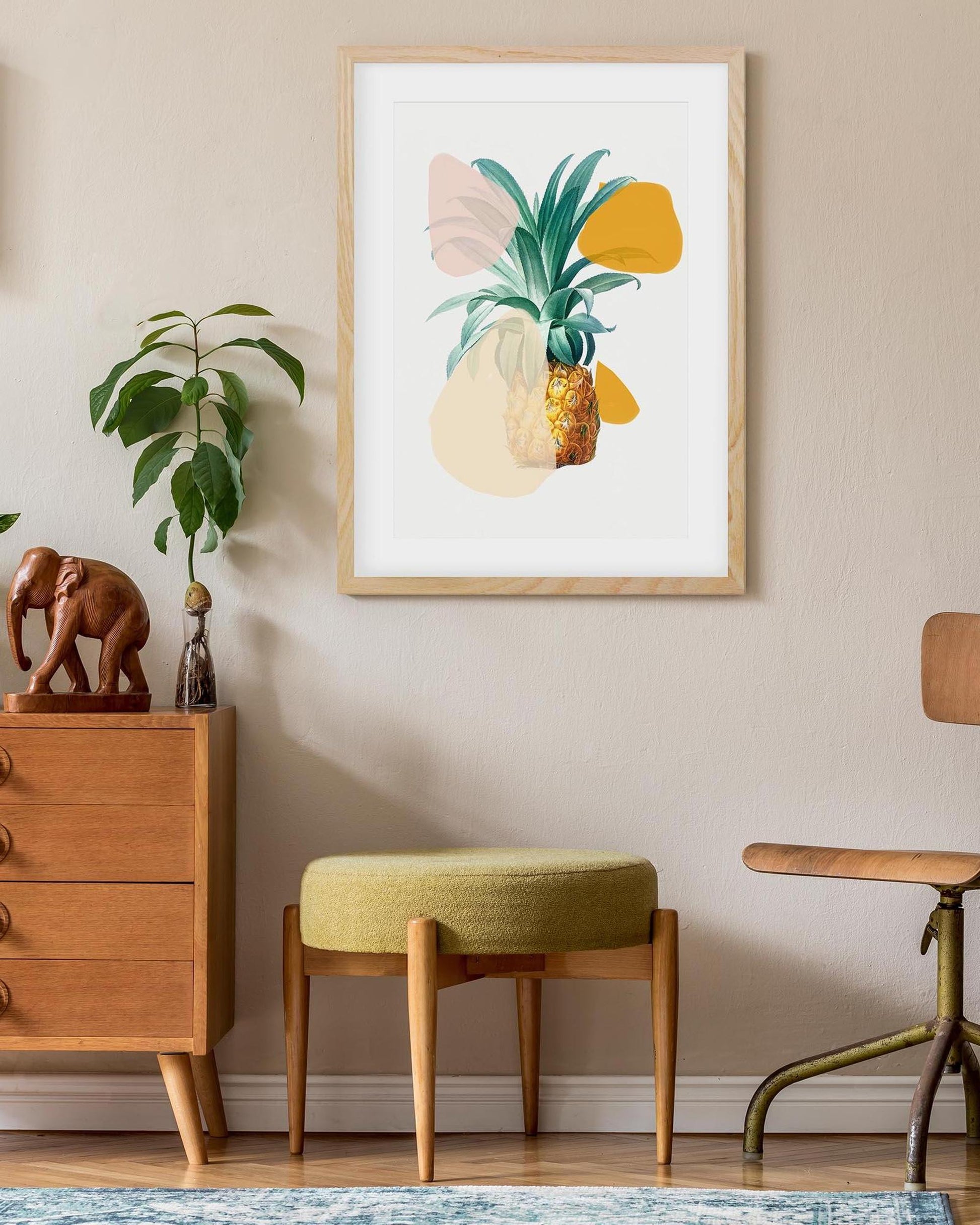 Framed artwork of a pineapple on a wall above a wooden cabinet and stool.
