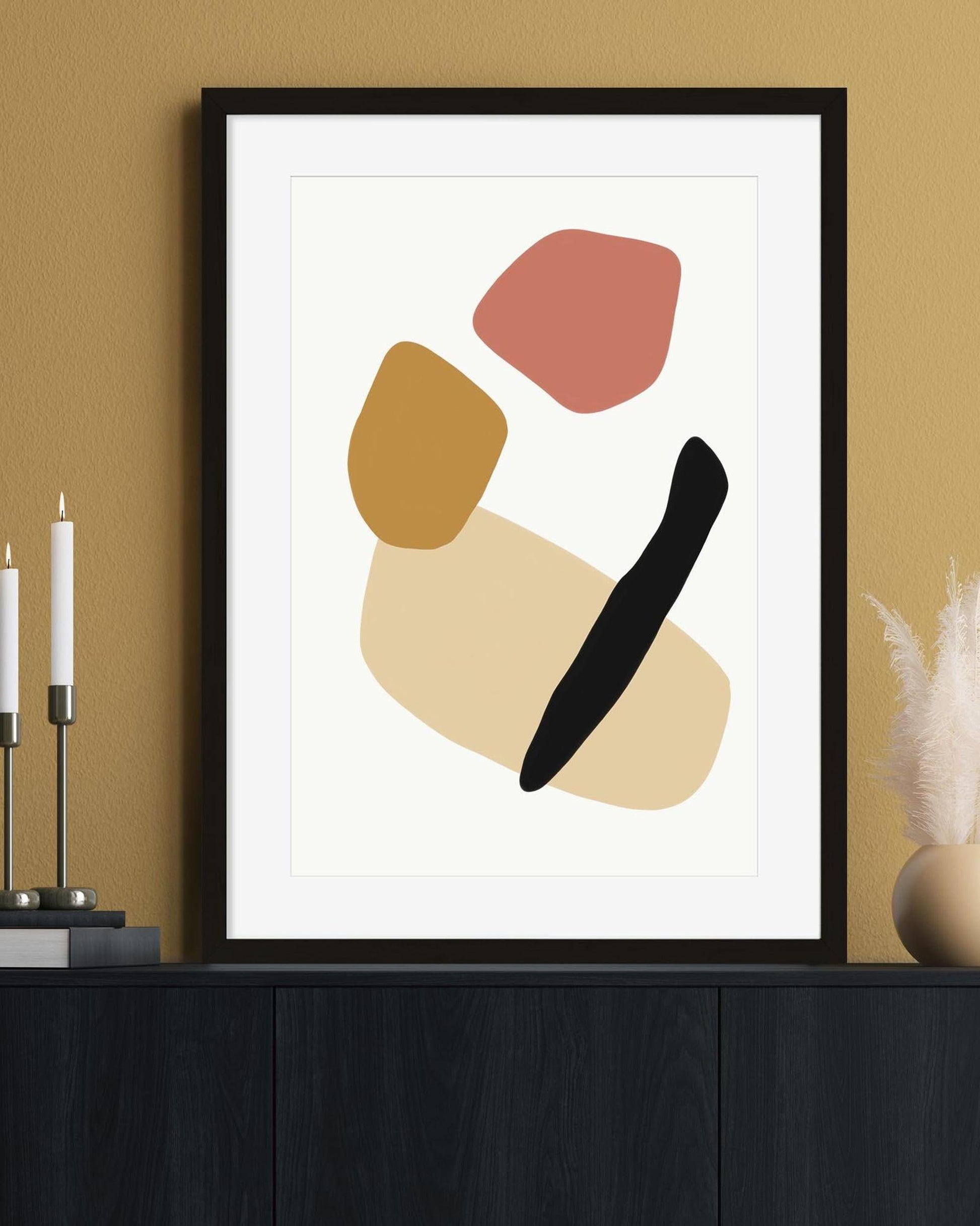 Framed abstract art print with colorful shapes on a beige wall.