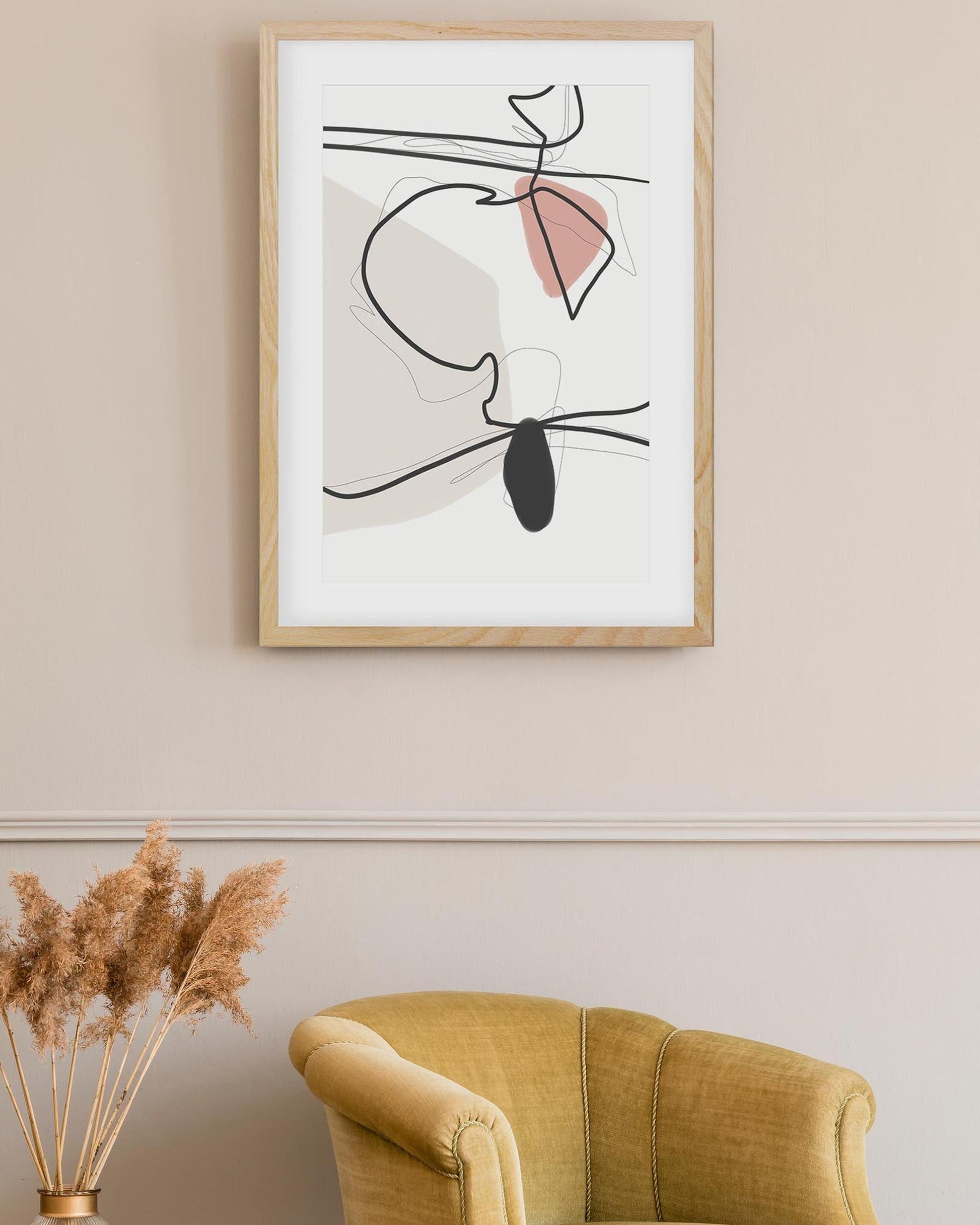 Framed abstract art on a wall with a yellow armchair and dried plants below.