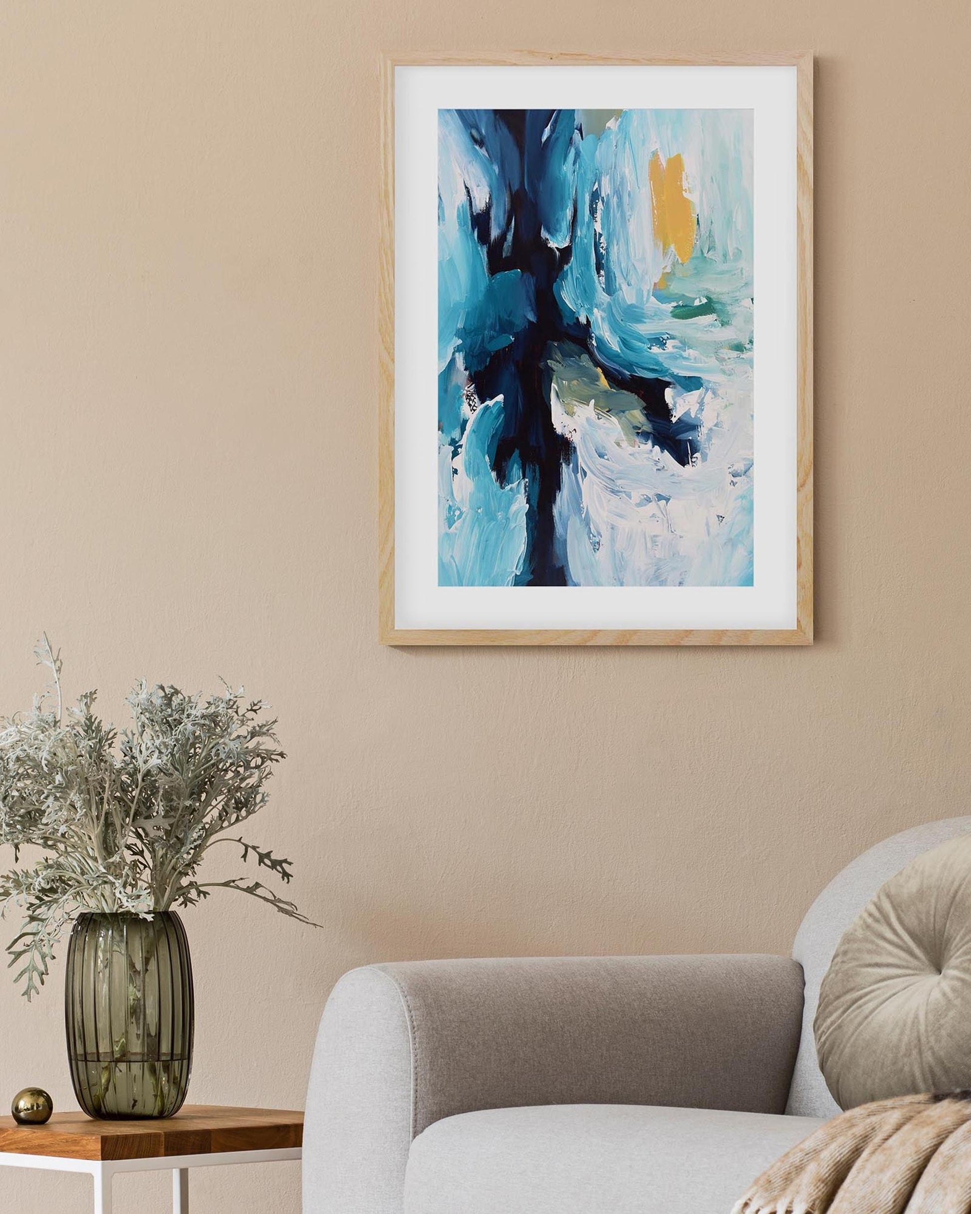 Abstract painting in a white frame on a beige wall above a sofa.