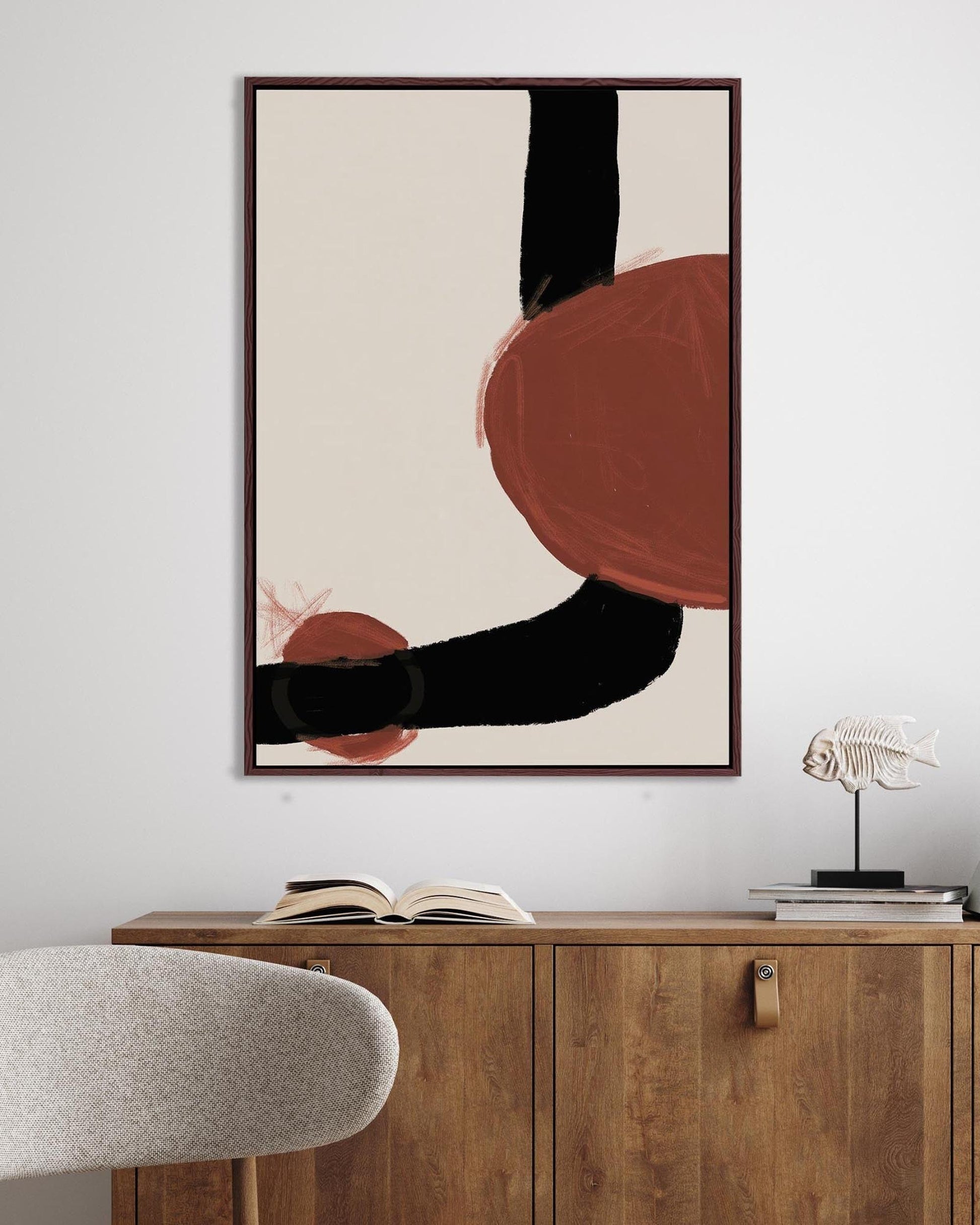 Abstract art print on a wall above a wooden cabinet with books and a lamp.