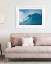Framed photograph of a blue wave above a beige sofa with a lamp on the left.