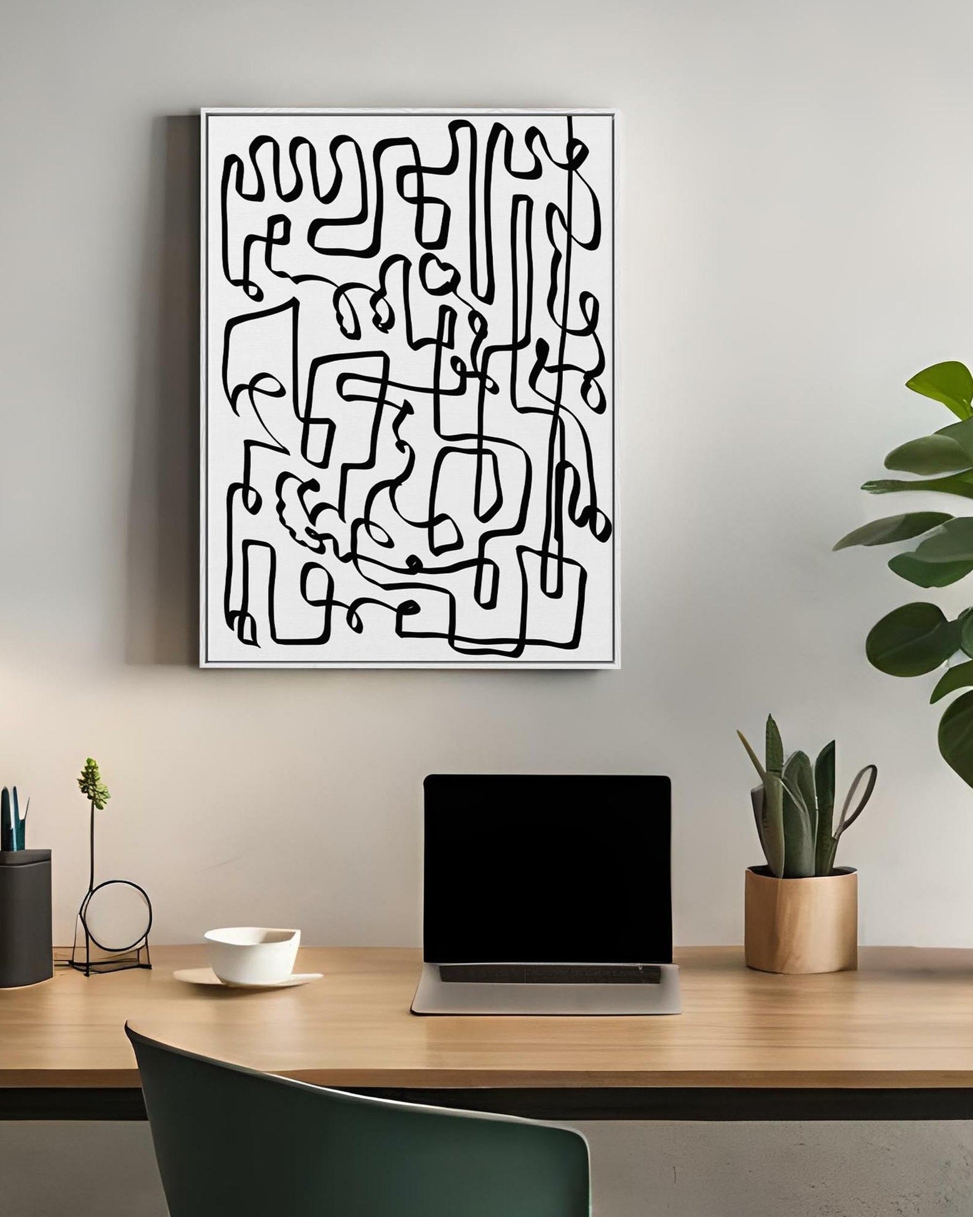 Abstract black and white artwork on a wall above a desk with a laptop and plants.