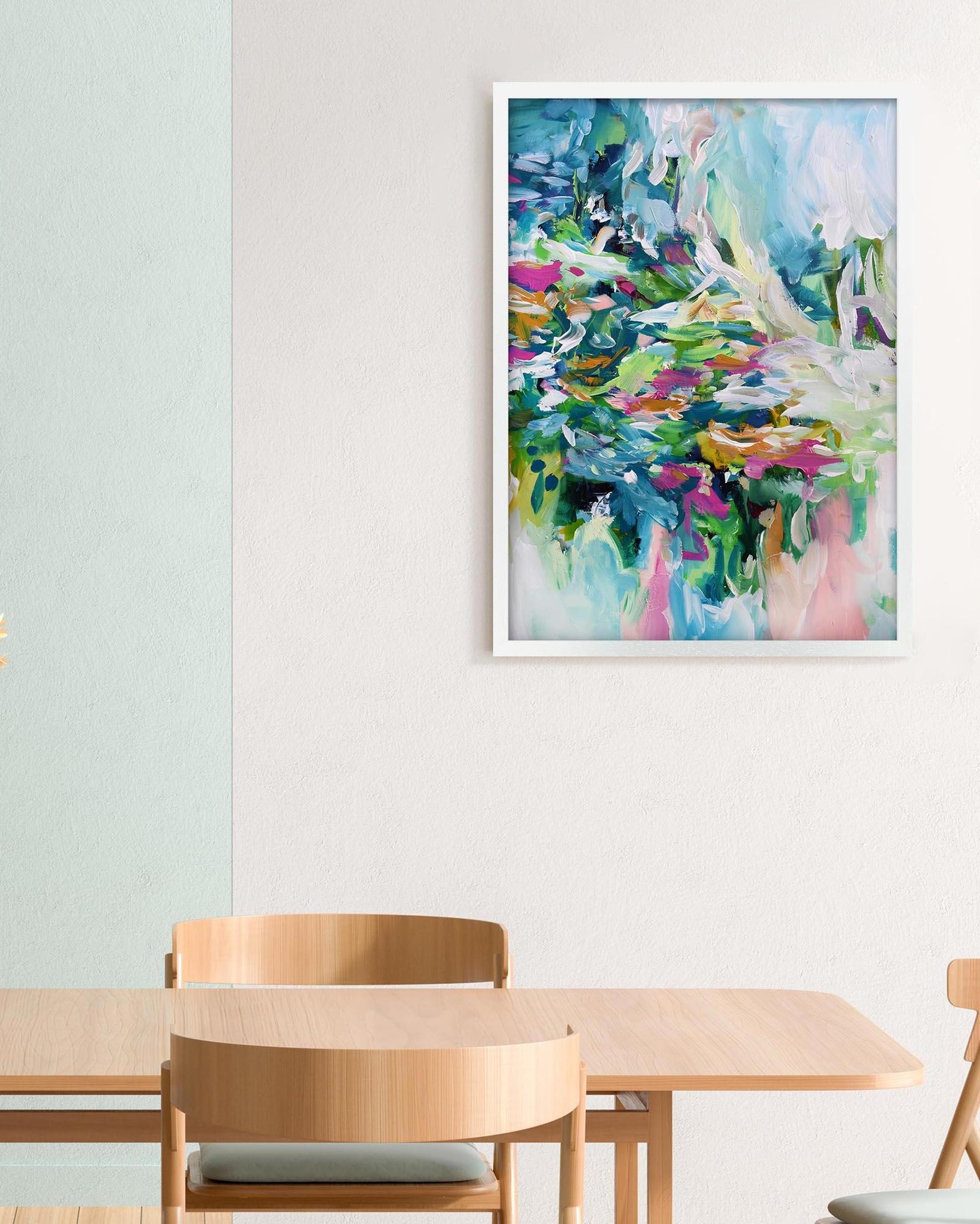 Colorful abstract painting in a white frame above a wooden table and chairs.
