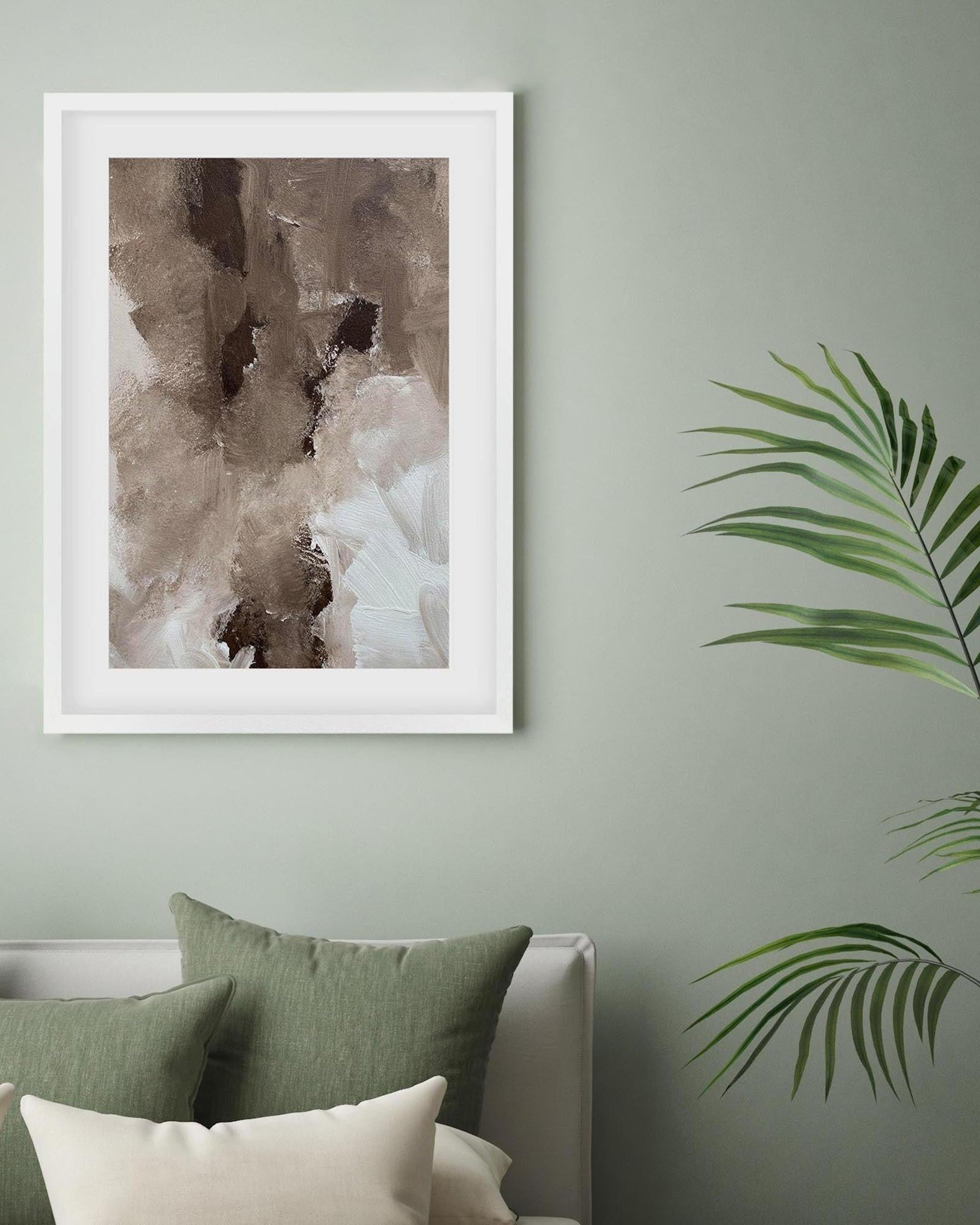 Framed abstract art piece on a wall with greenery and pillows below.