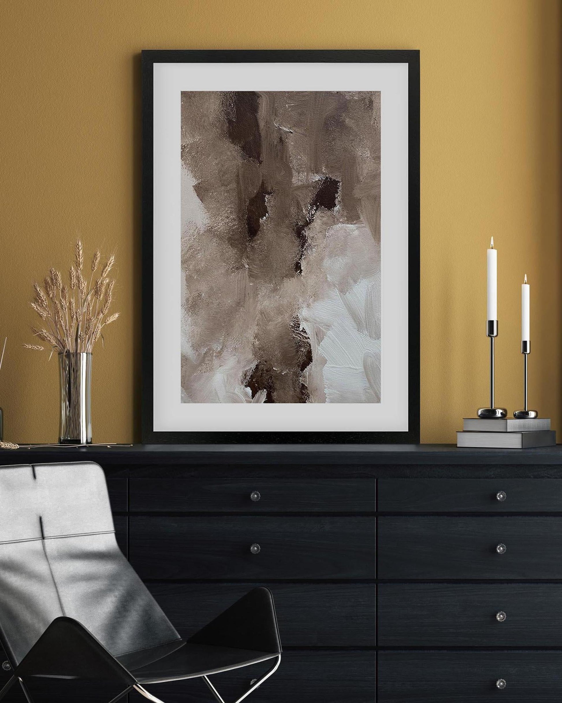 Framed abstract art piece on a wall above a black dresser with decorative items.