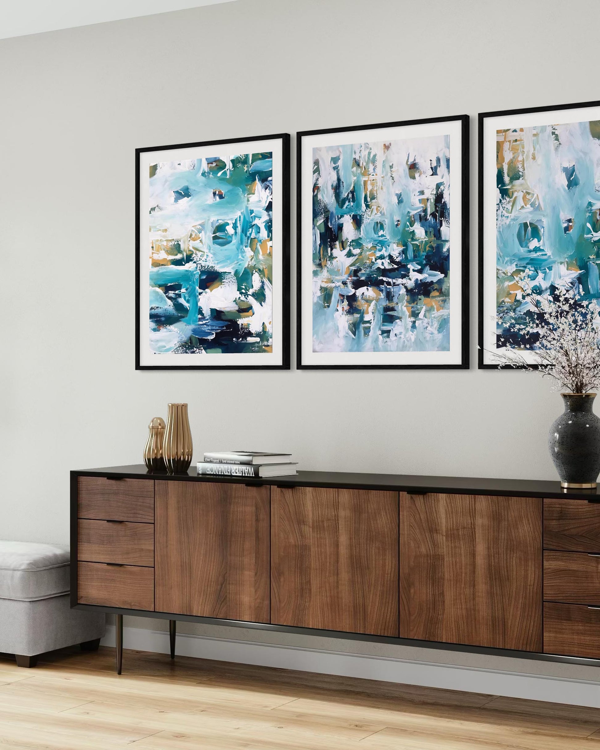 Three abstract paintings on a wall above a wooden console table.