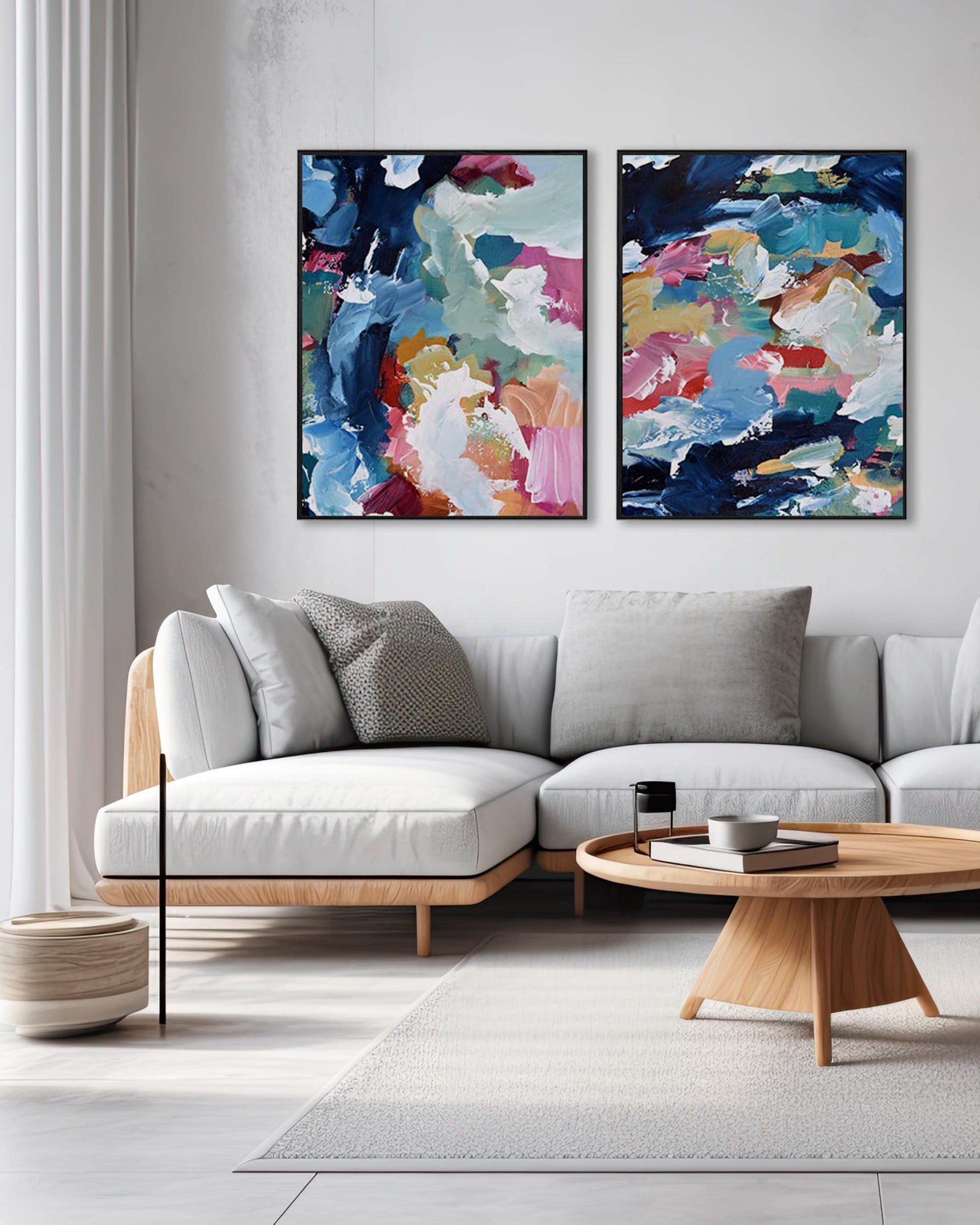 A set of two abstract canvas paintings featuring geometric patterns with a combination of blue, pink, brown, white, and black colors, displayed above a white sofa in a living room setting.
