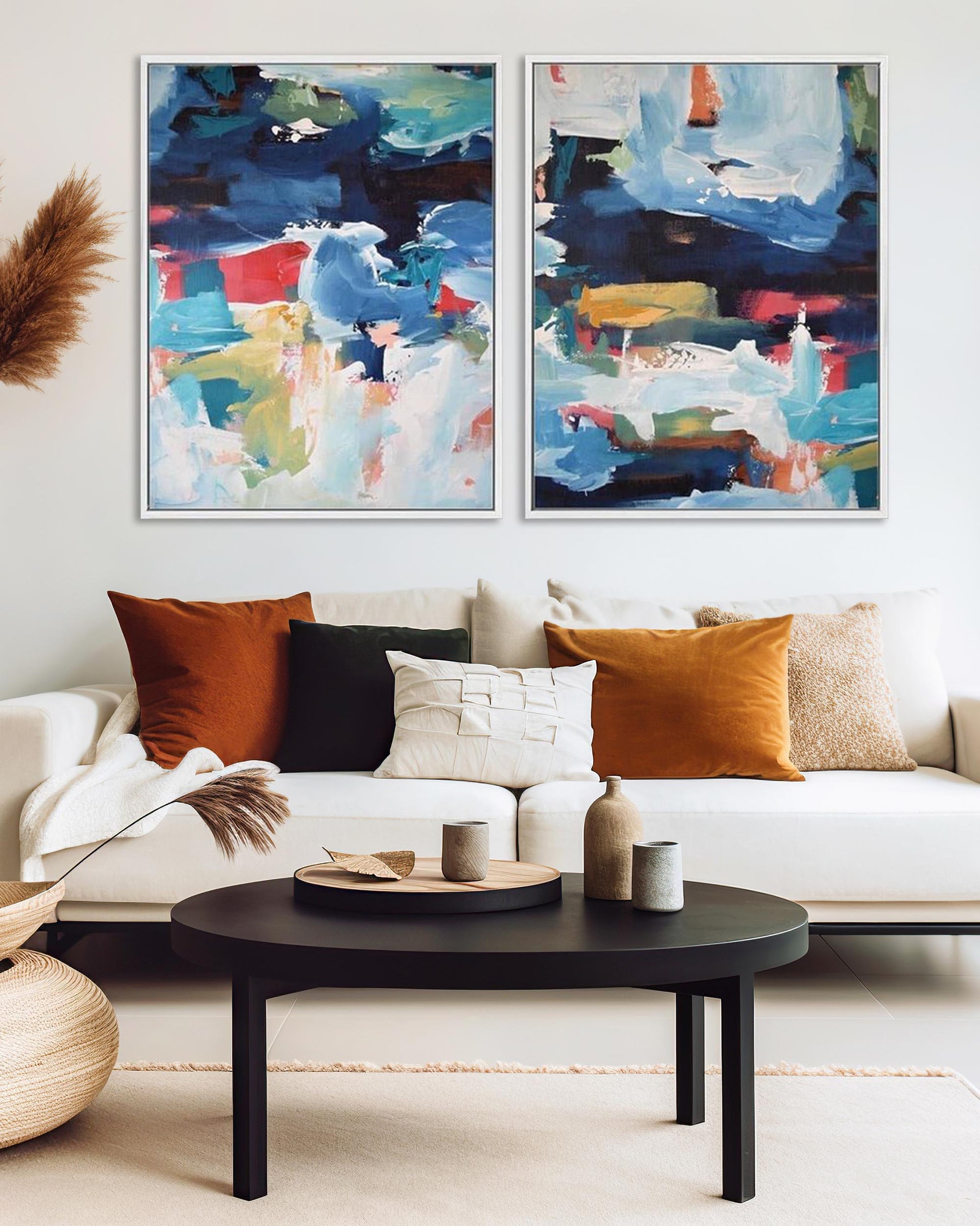 A set of two abstract canvas paintings featuring geometric patterns in blue, black, and colorful tones, displayed above a white sofa in a living room setting.