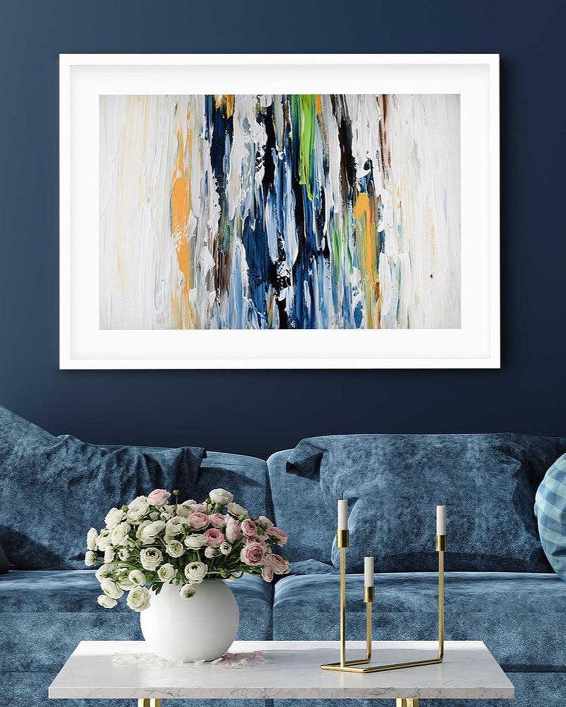 Abstract art print on a wall above a blue sofa with a coffee table and decorative items.
