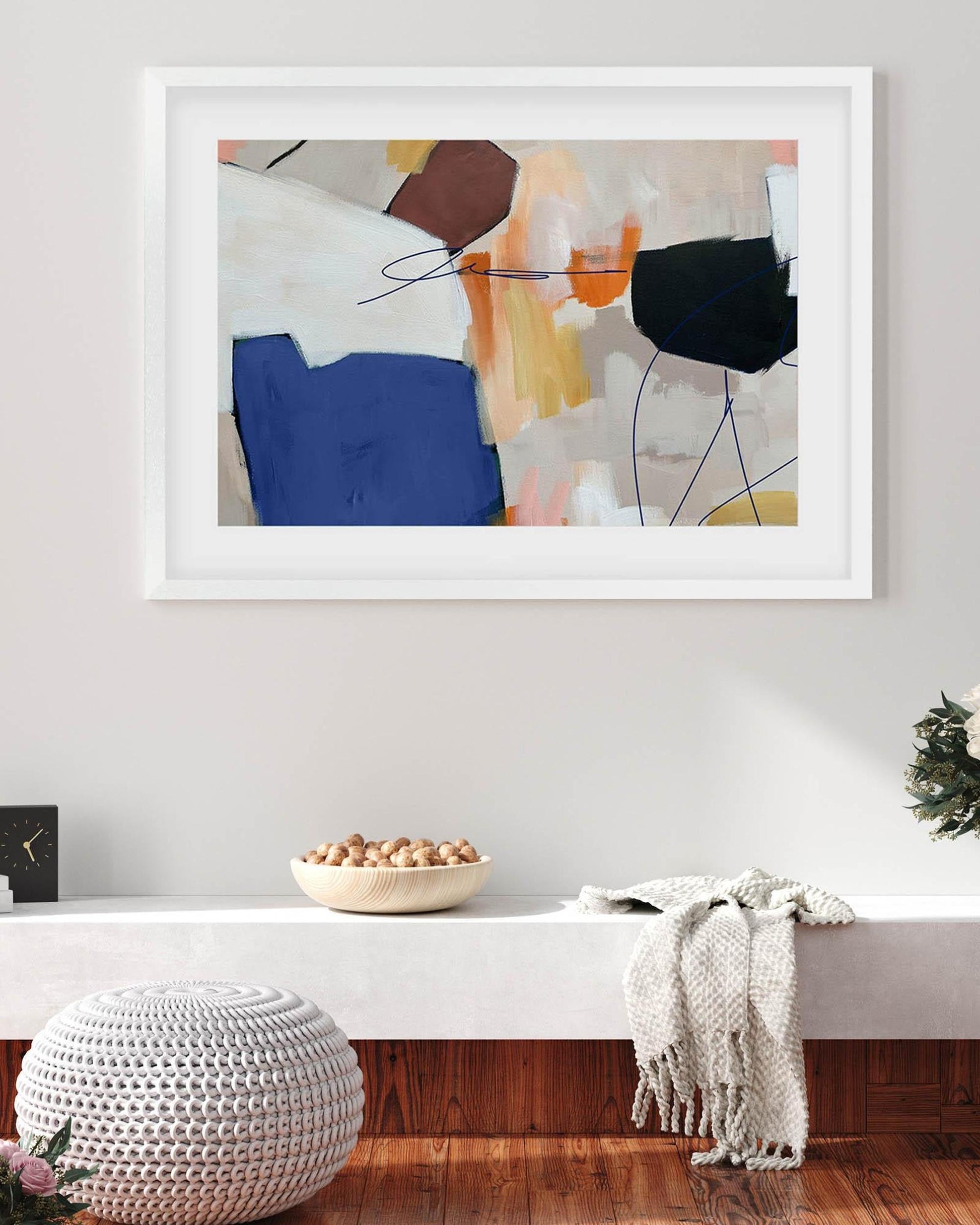 Framed abstract art piece on a wall above a white console table with decorative items.