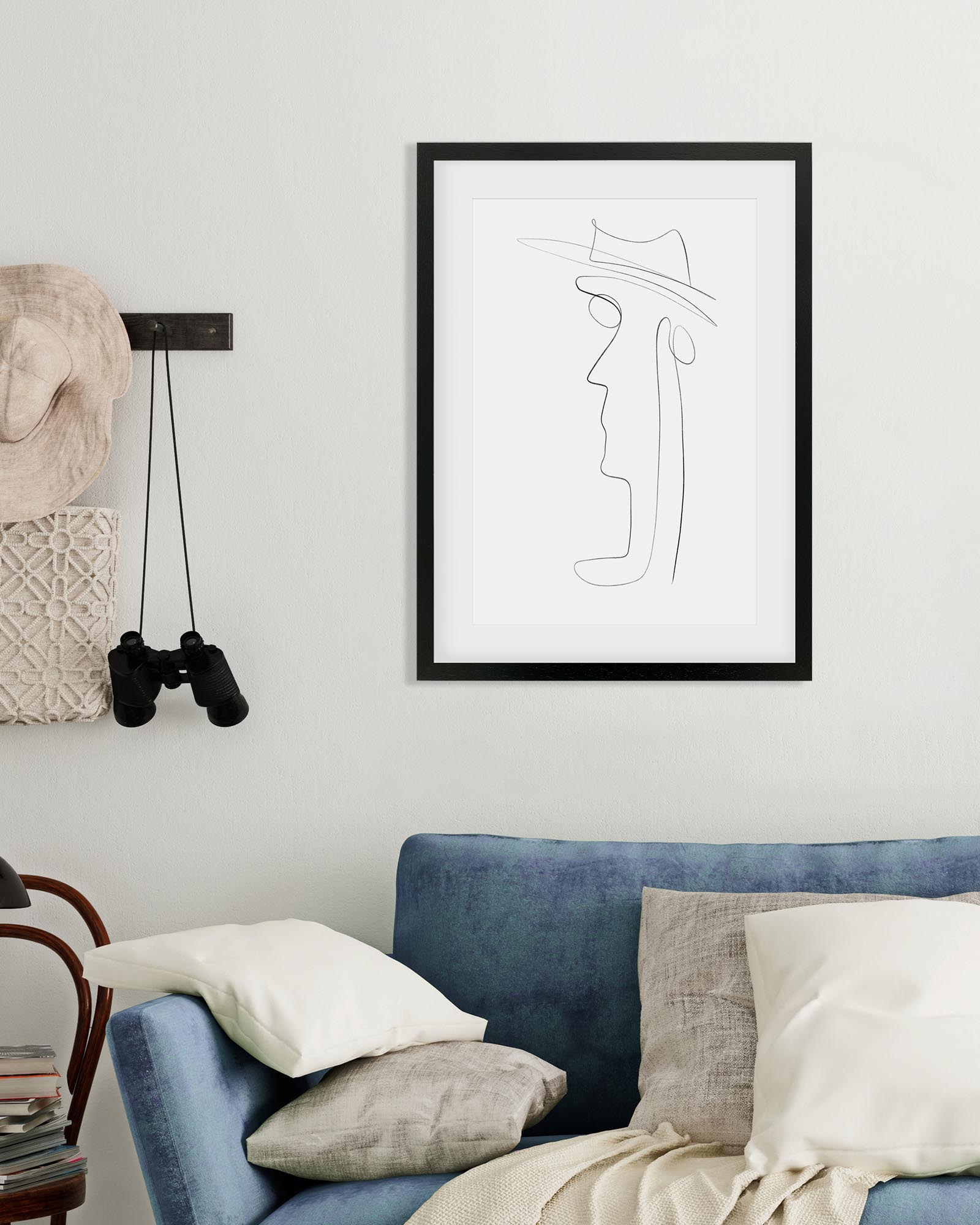 Framed black and white line art of a face on a wall above a blue sofa.