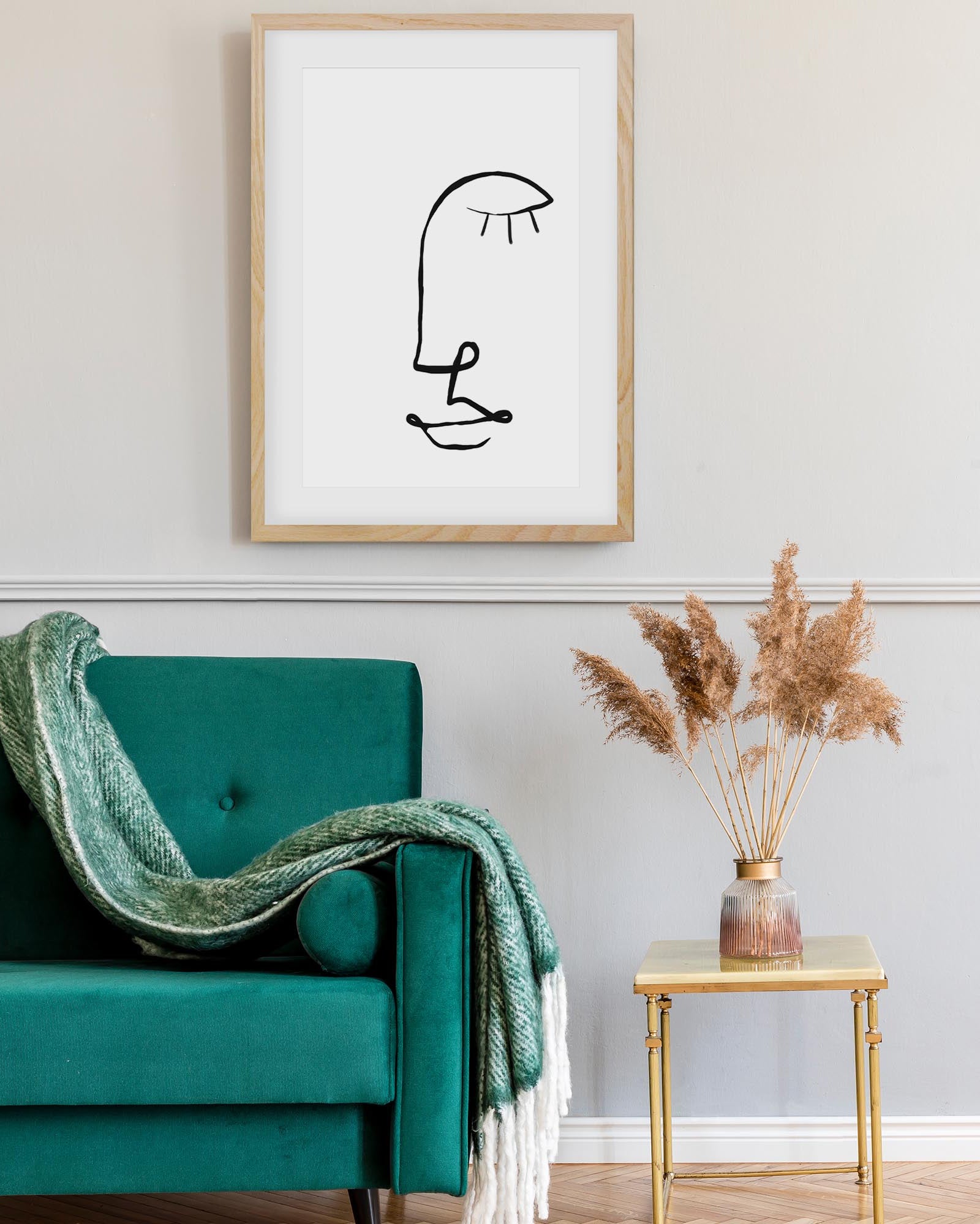 Framed abstract artwork above a teal armchair with a green blanket in a living room setting.