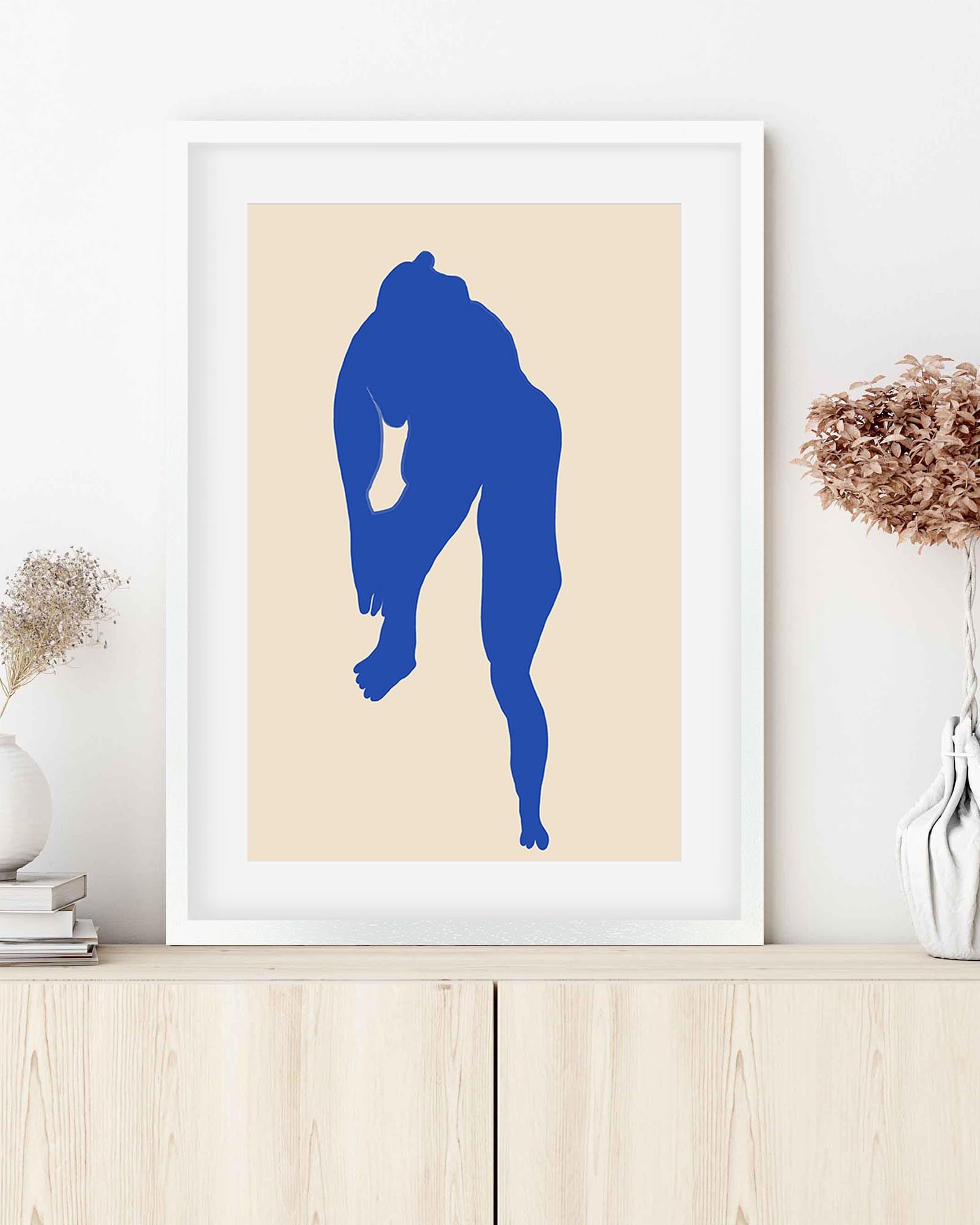 Framed artwork with a blue silhouette on a beige background, displayed on a wooden surface.
