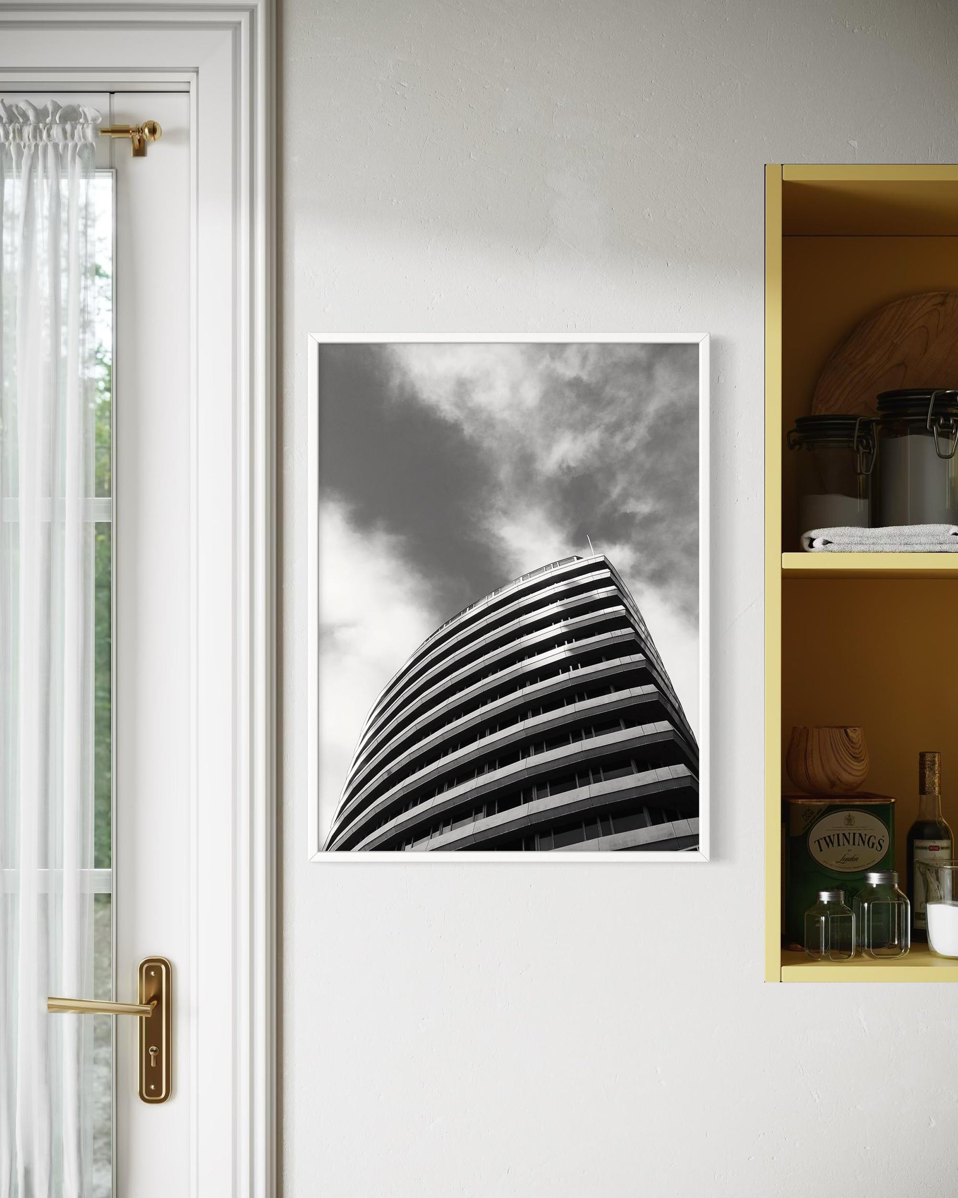 Poster of a modern building on a white wall next to a door with a gold handle.