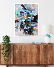 Abstract painting on a wall above a wooden cabinet with a lamp and plant.