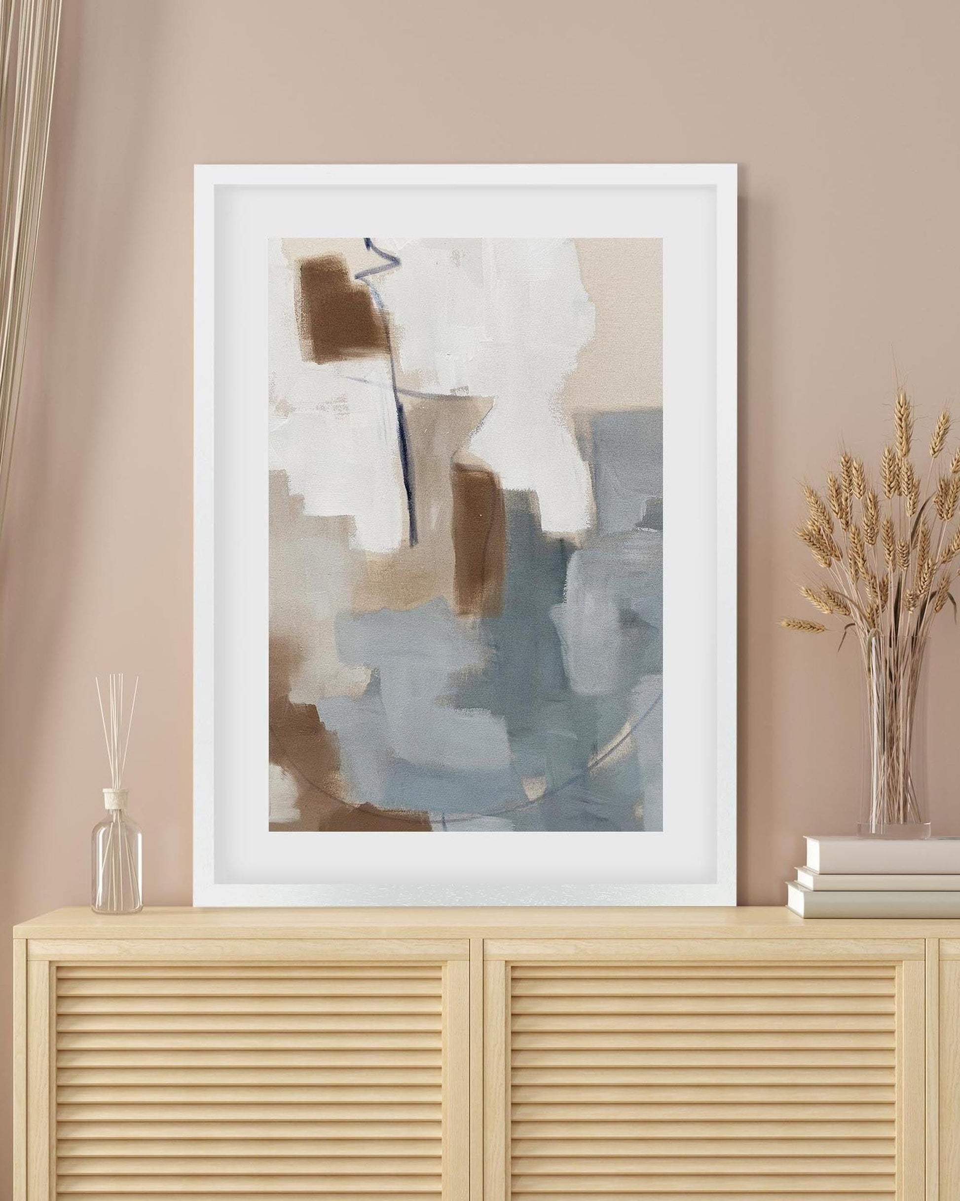 Abstract art print in a white frame on a beige wall above a wooden cabinet.