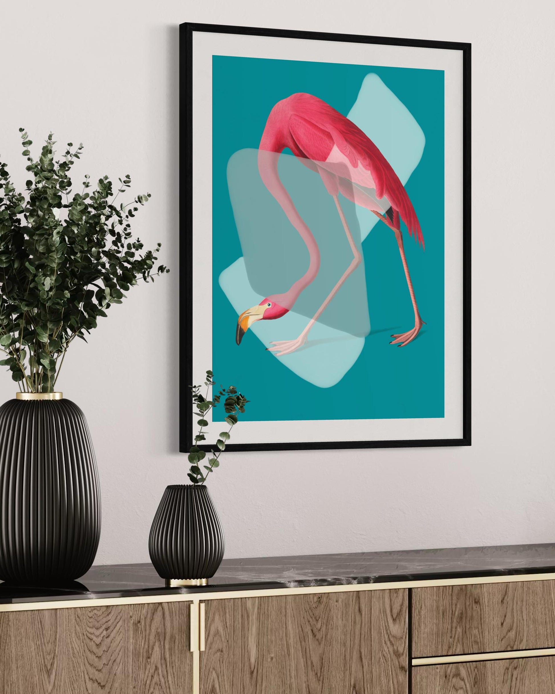 Framed artwork of a pink flamingo on a teal background, displayed on a wall above a wooden cabinet with black vases.
