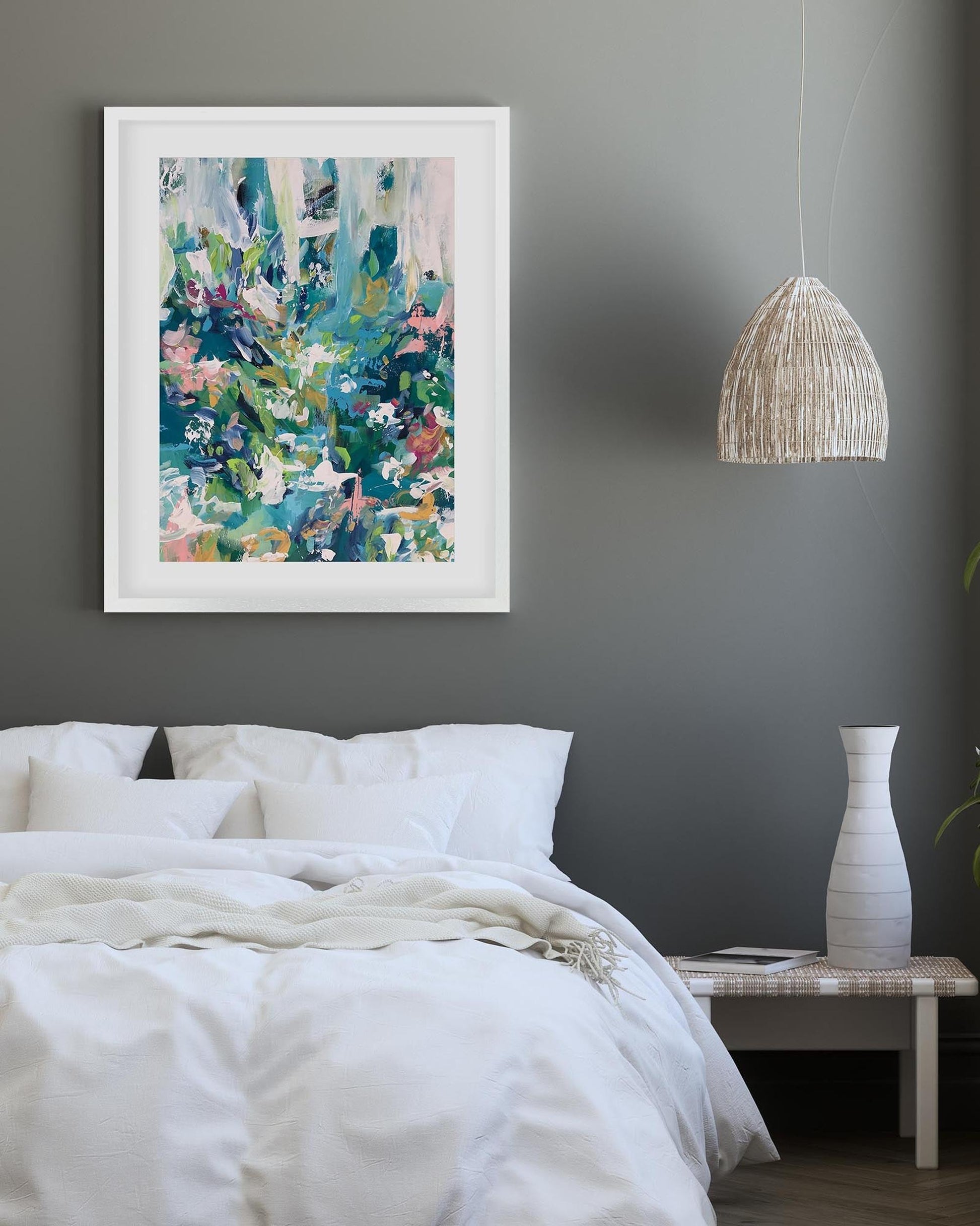 Framed abstract art above a bed in a bedroom with a pendant light and vase.