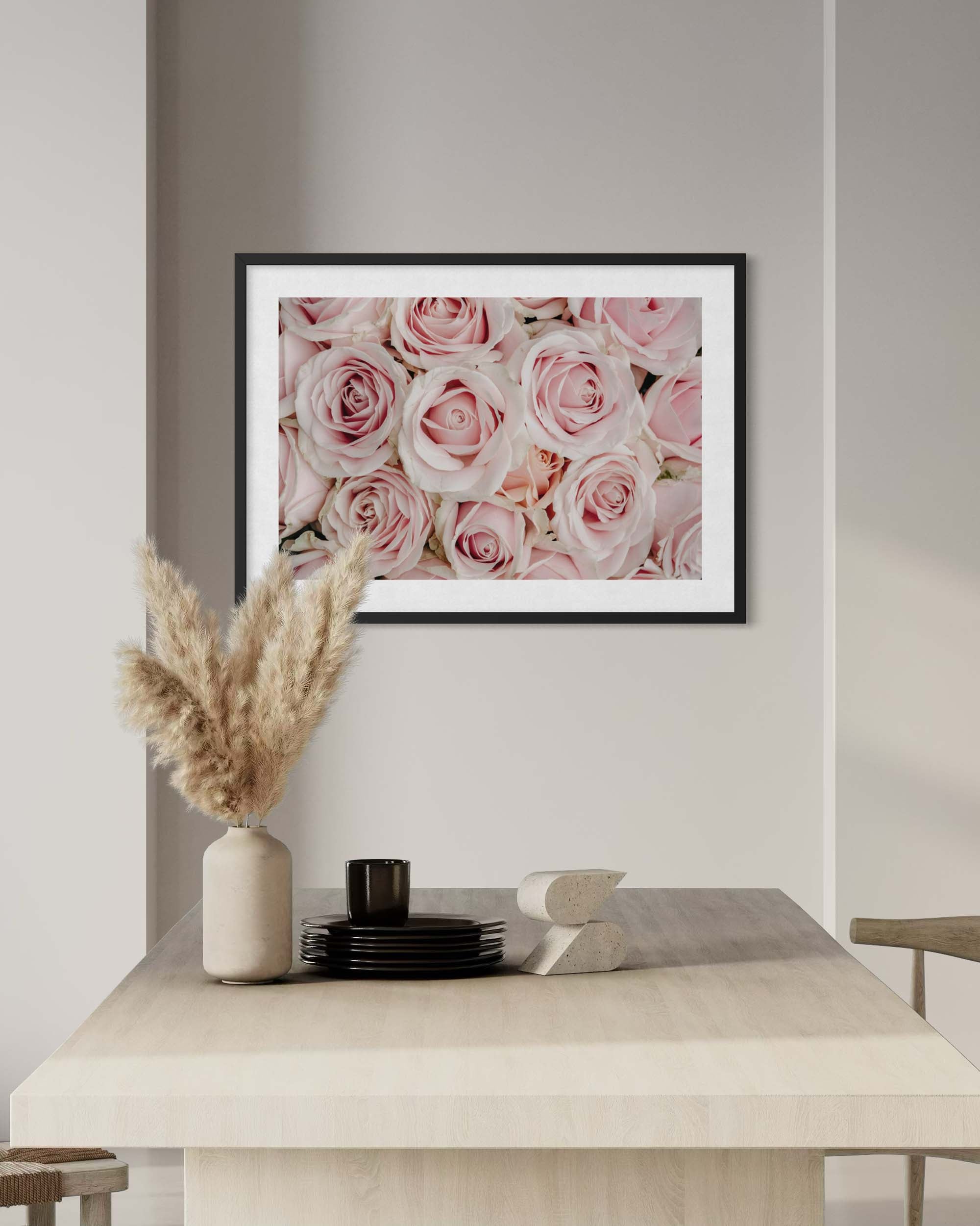 Framed artwork of pink roses above a dining table with decor items.