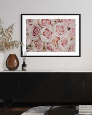 Framed picture of pink roses on a wall above a black cabinet.